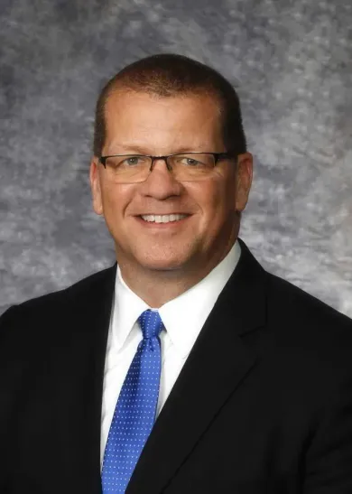 A man in a suit and tie is smiling in front of a wooden wall.