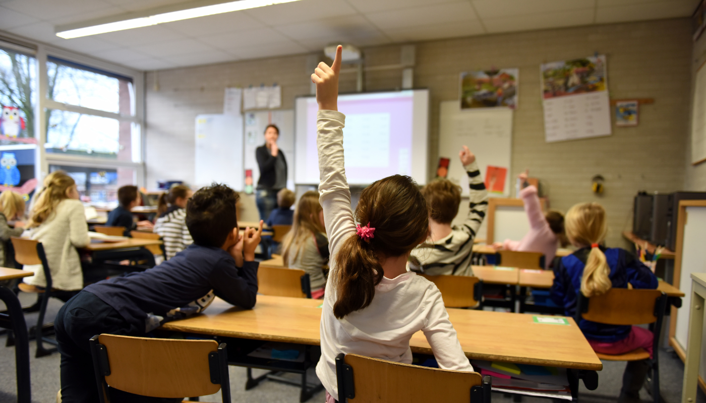 A girl is raising her hand in a classroom to answer a question.