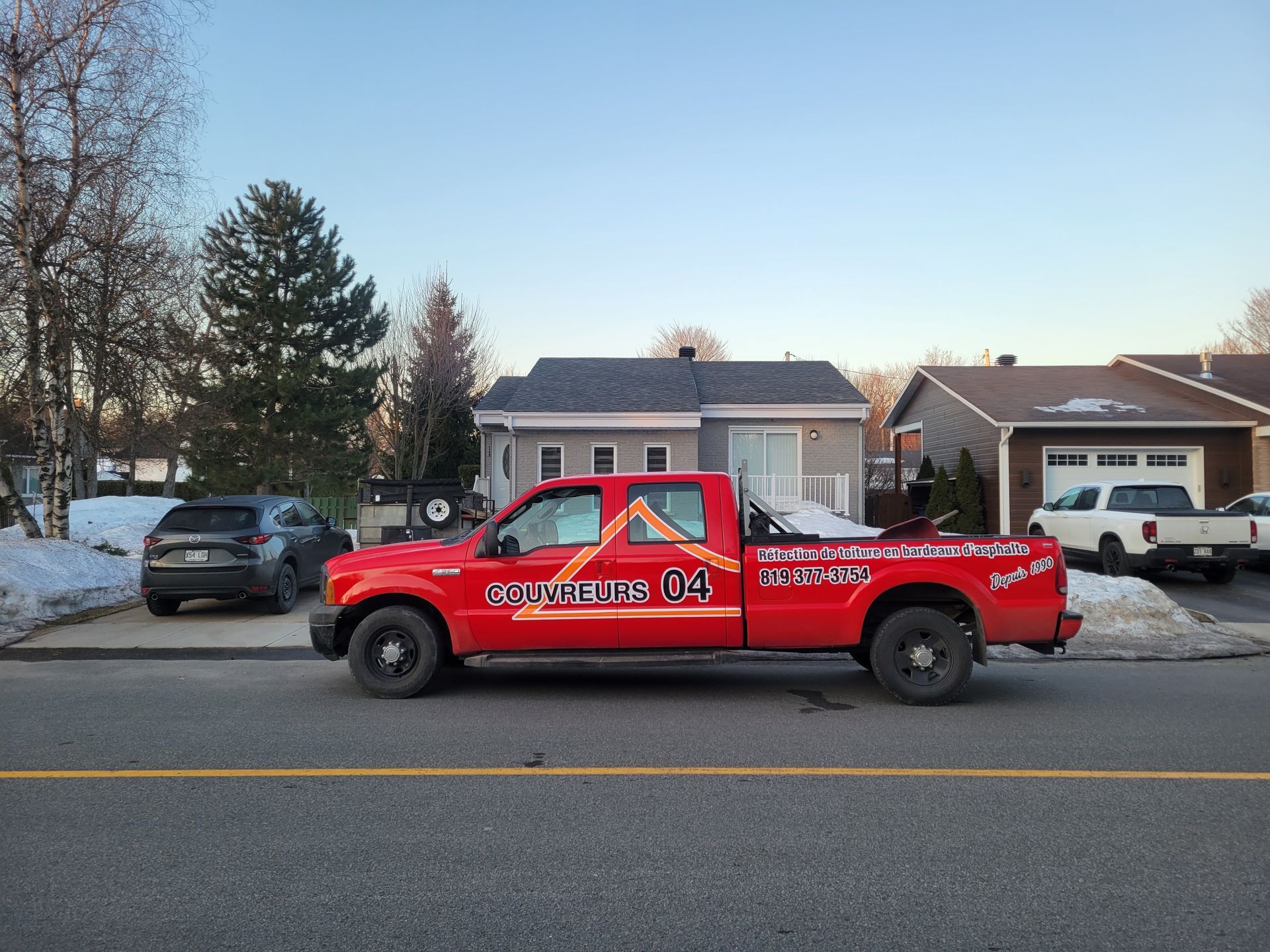 Un camion rouge est garé sur le bord de la route devant une maison.
