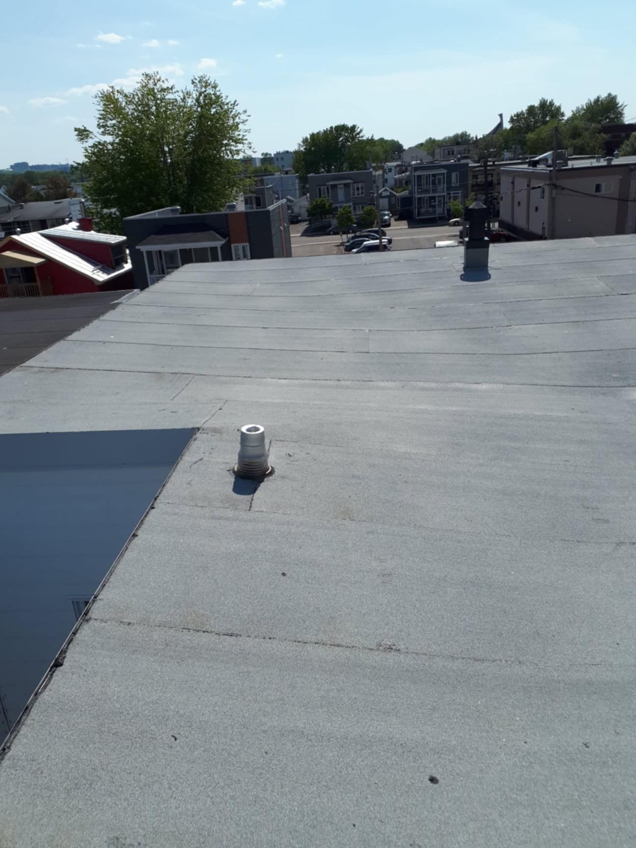 Un toit plat et gris avec deux évents et un arrière-plan de paysage urbain par une journée ensoleillée.