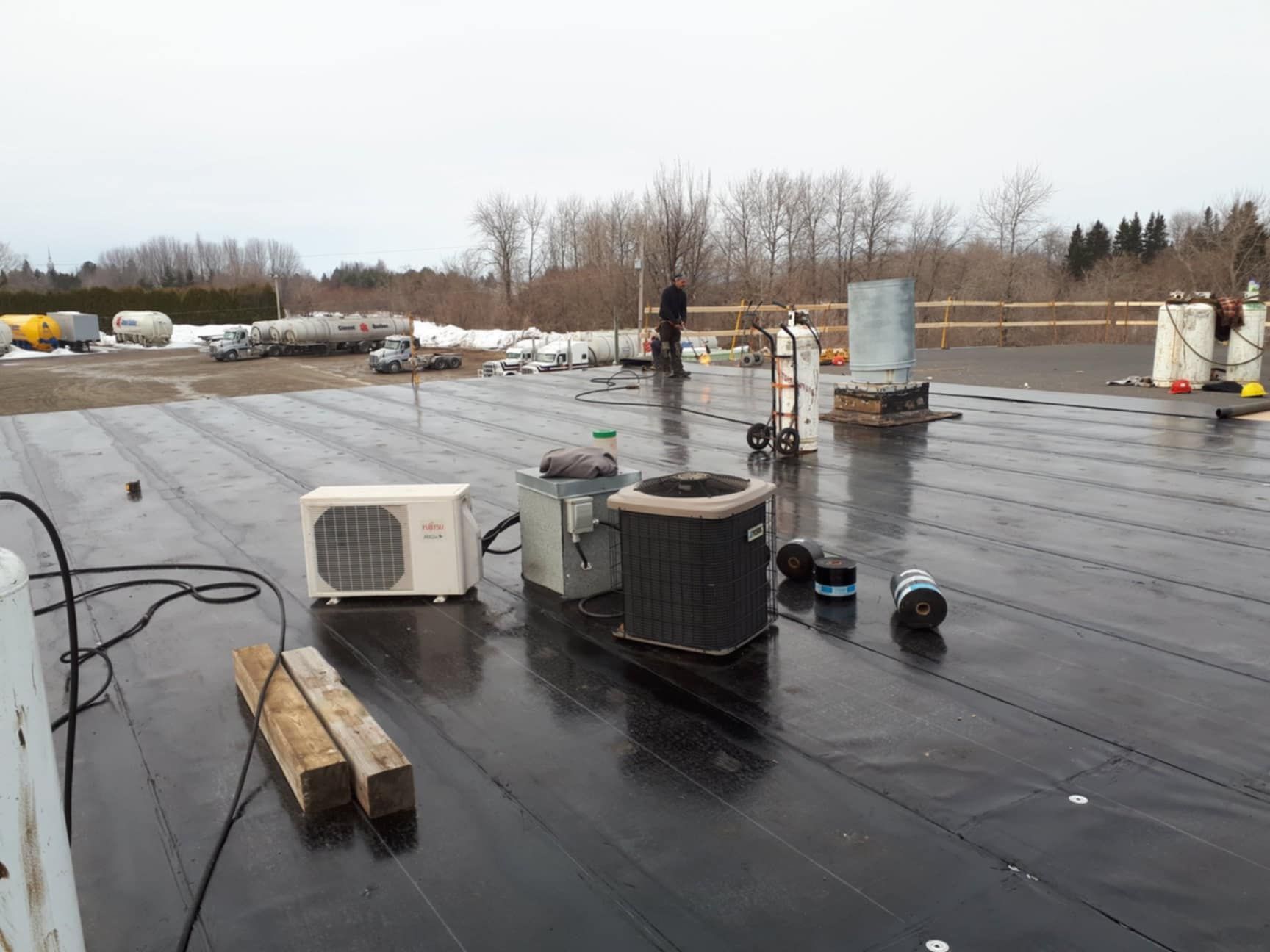 Toit noir avec unités de CVC, outils et personne au travail. Extérieur, journée nuageuse.