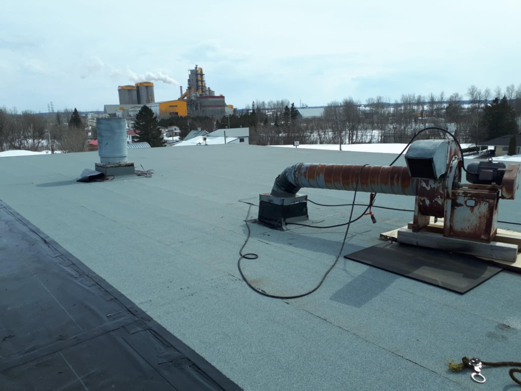 Toit avec équipement de ventilation, bâtiment industriel en arrière-plan, un peu de neige.