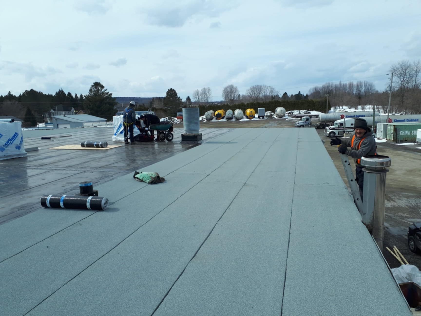 Couvreurs installant un toit plat sur un bâtiment avec un ciel dégagé.