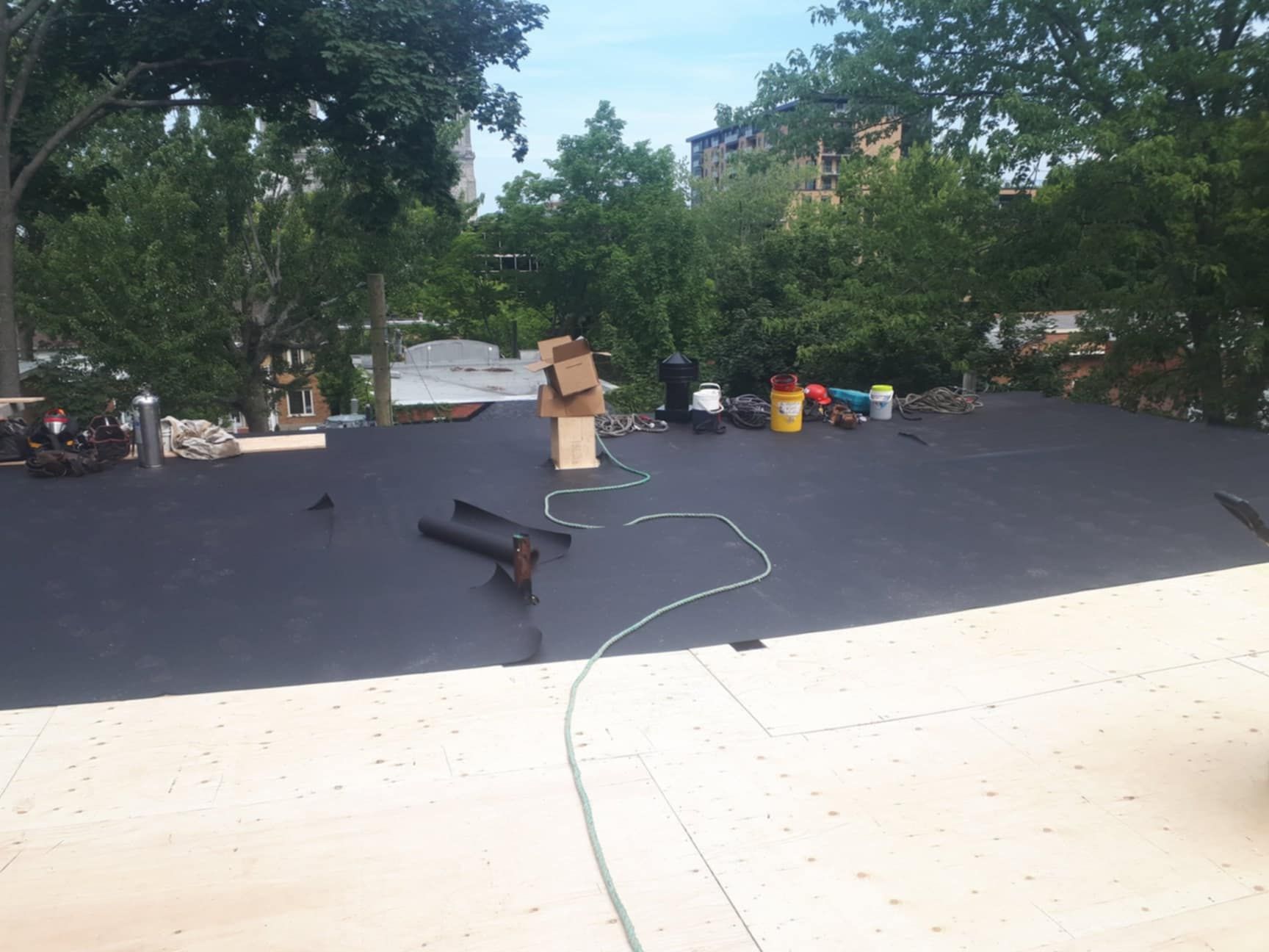 Toit plat avec équipement, outils, boîte en carton et arbres en arrière-plan par une journée ensoleillée.