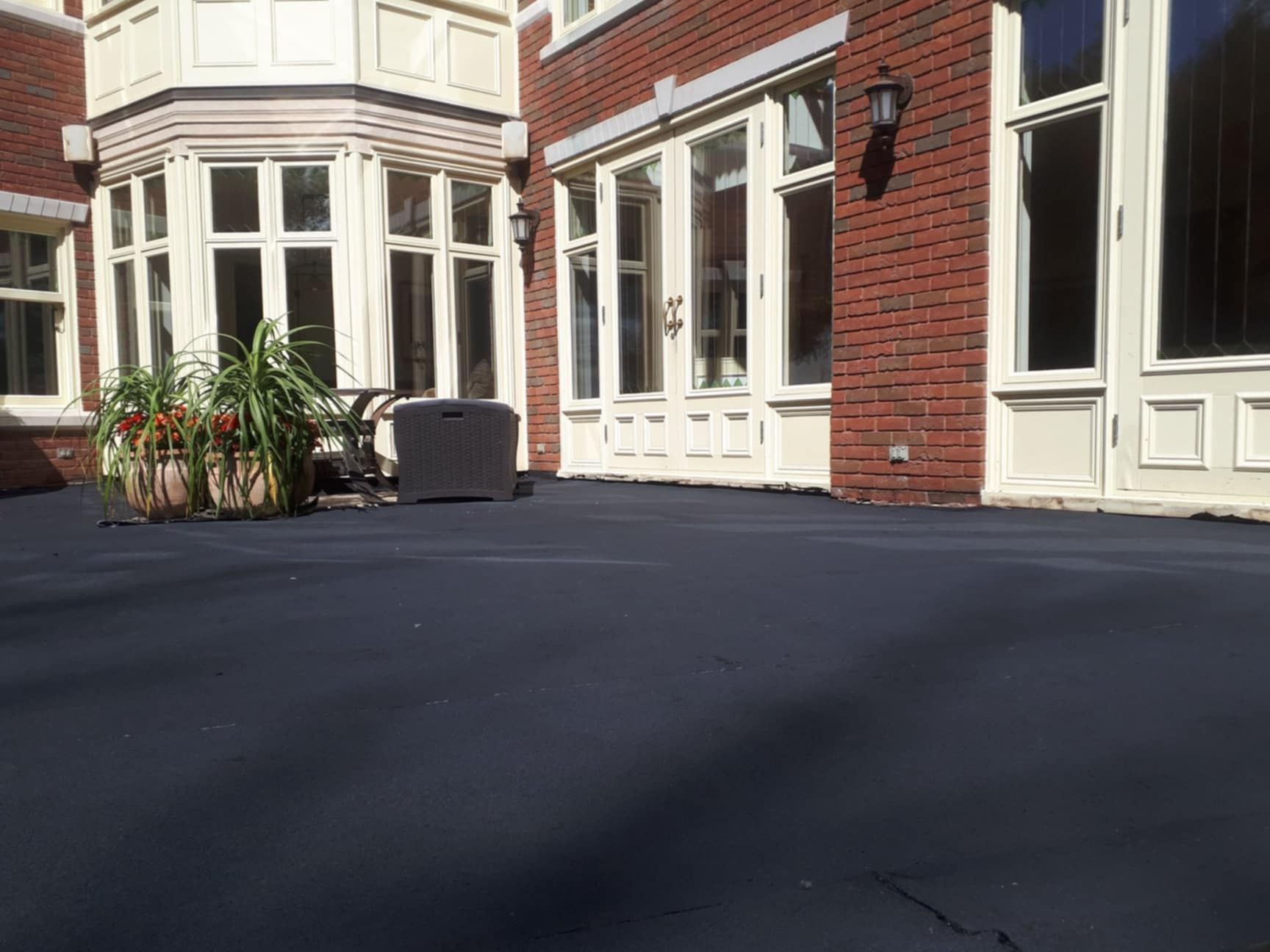 Patio peint en noir à côté d'une maison en briques rouges avec des fenêtres et des portes bordées de blanc.