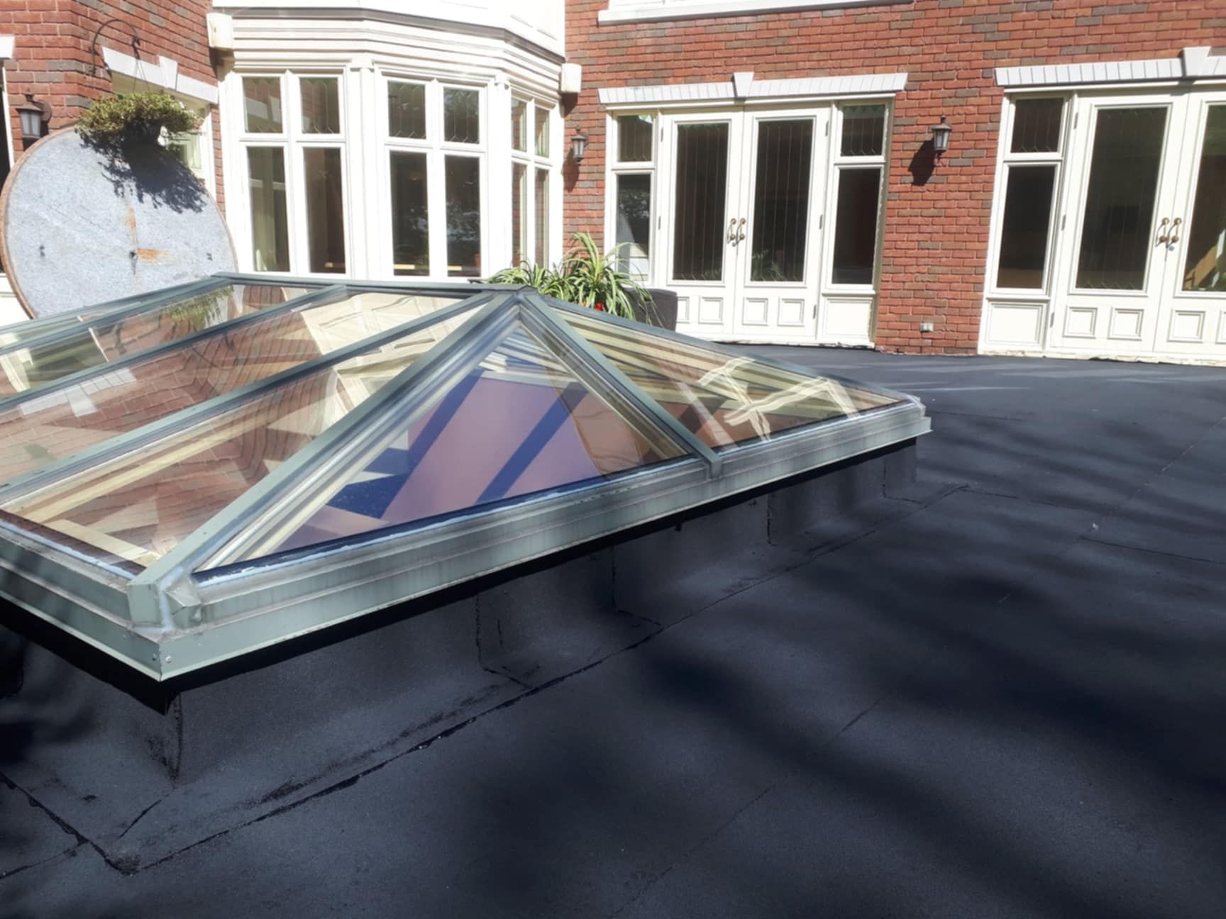 Un toit plat noir avec une lucarne en verre et un bâtiment en briques en arrière-plan.