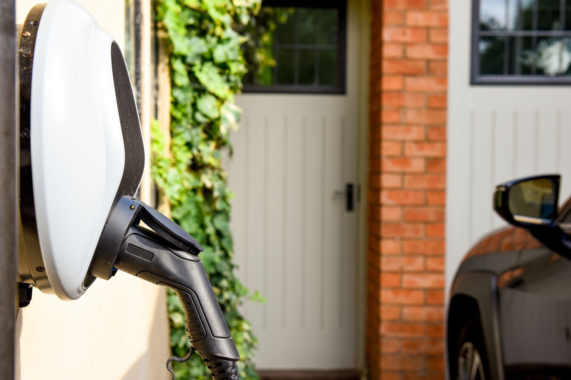 Electric vehicle charging station on a beige wall, cable plugged into car, near a doorway.