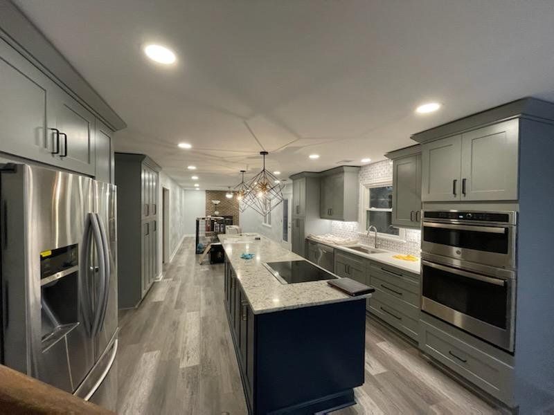 Modern kitchen with grey cabinets, stainless steel appliances, blue island, and recessed lighting.