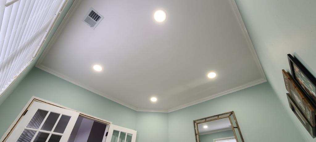 Low-angle shot of a white ceiling with recessed lights and crown molding.  Pale green walls, a window, and a mirror are visible.