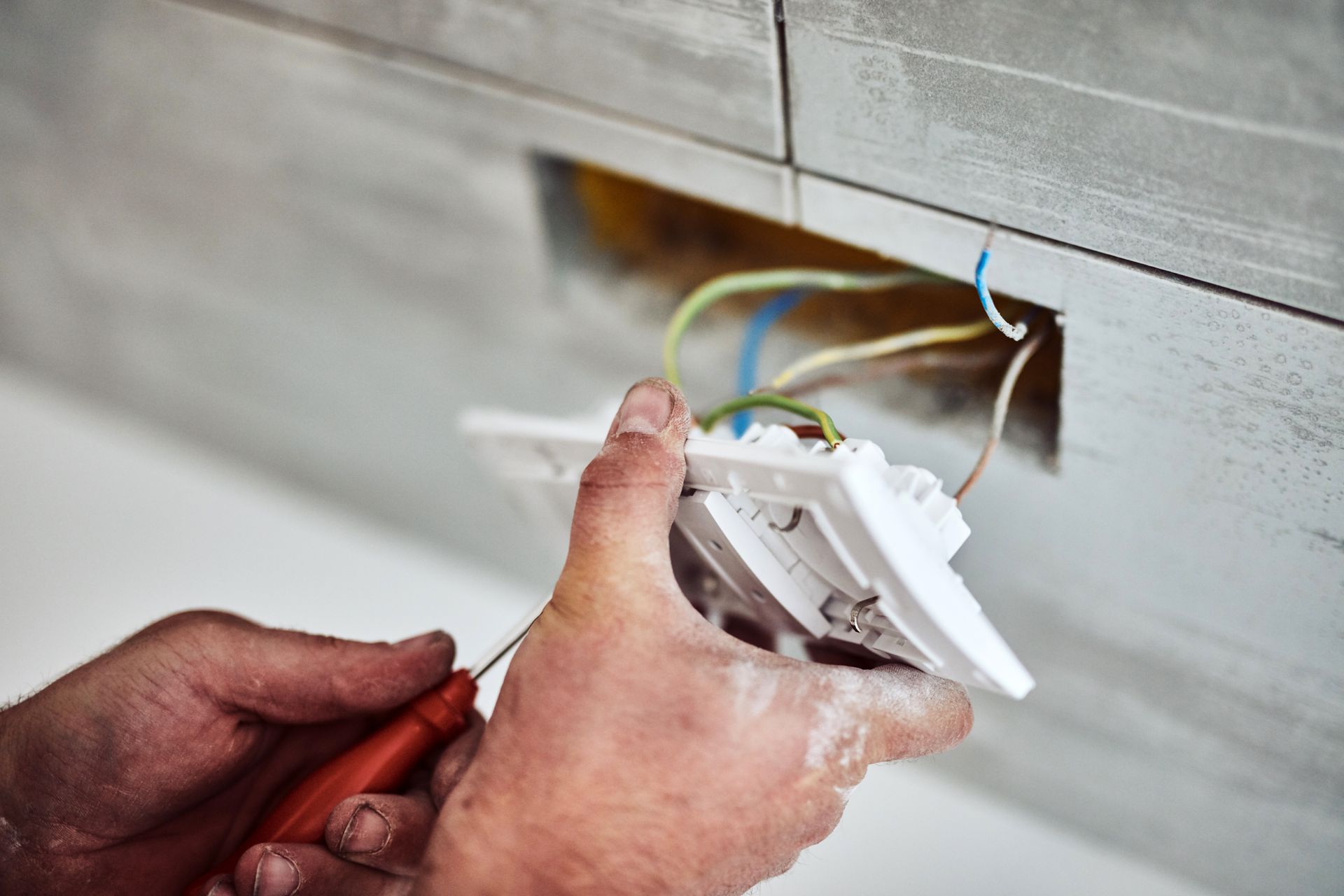 Technician repairing an electrical outlet with exposed wires using a screwdriver.
