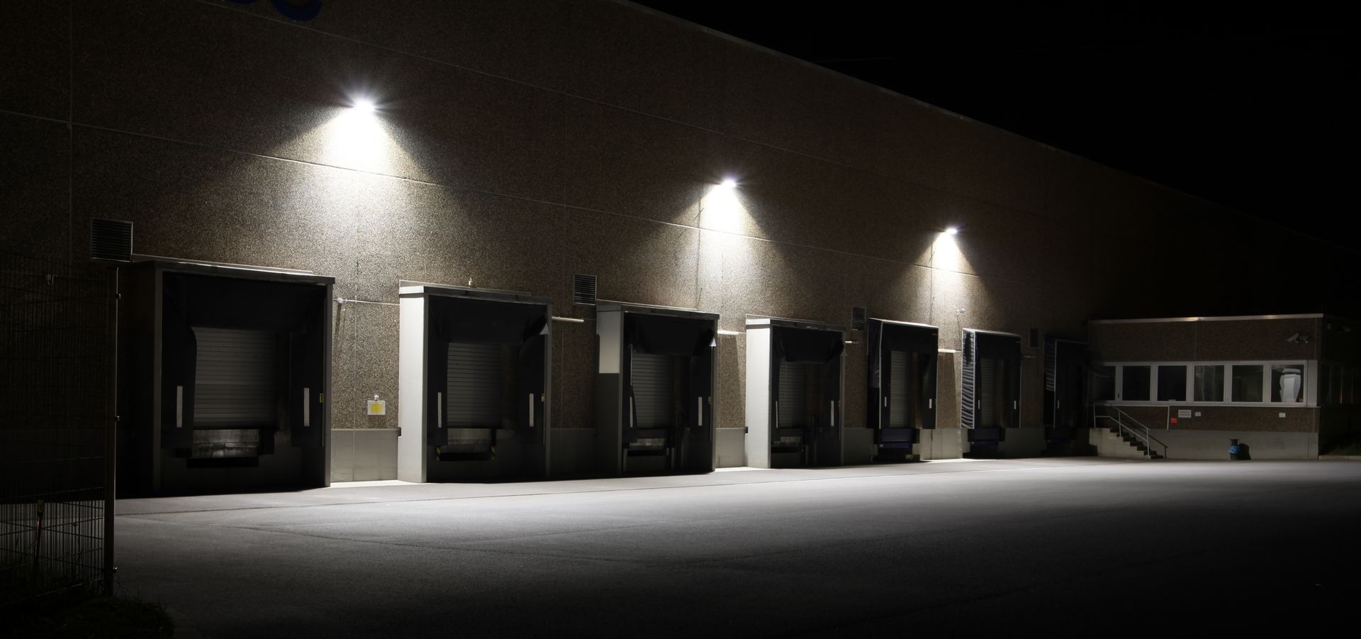 Exterior of a warehouse at night, illuminated by overhead lights shining on loading docks.