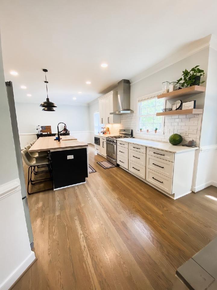 Bright kitchen with white cabinets, black island, stainless steel appliances, and wood floors.