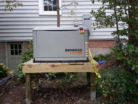 Generac generator on a wooden platform next to a house, with wiring visible.