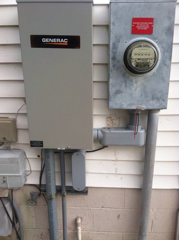 Gray Generac generator and electrical meter boxes on a white siding wall.