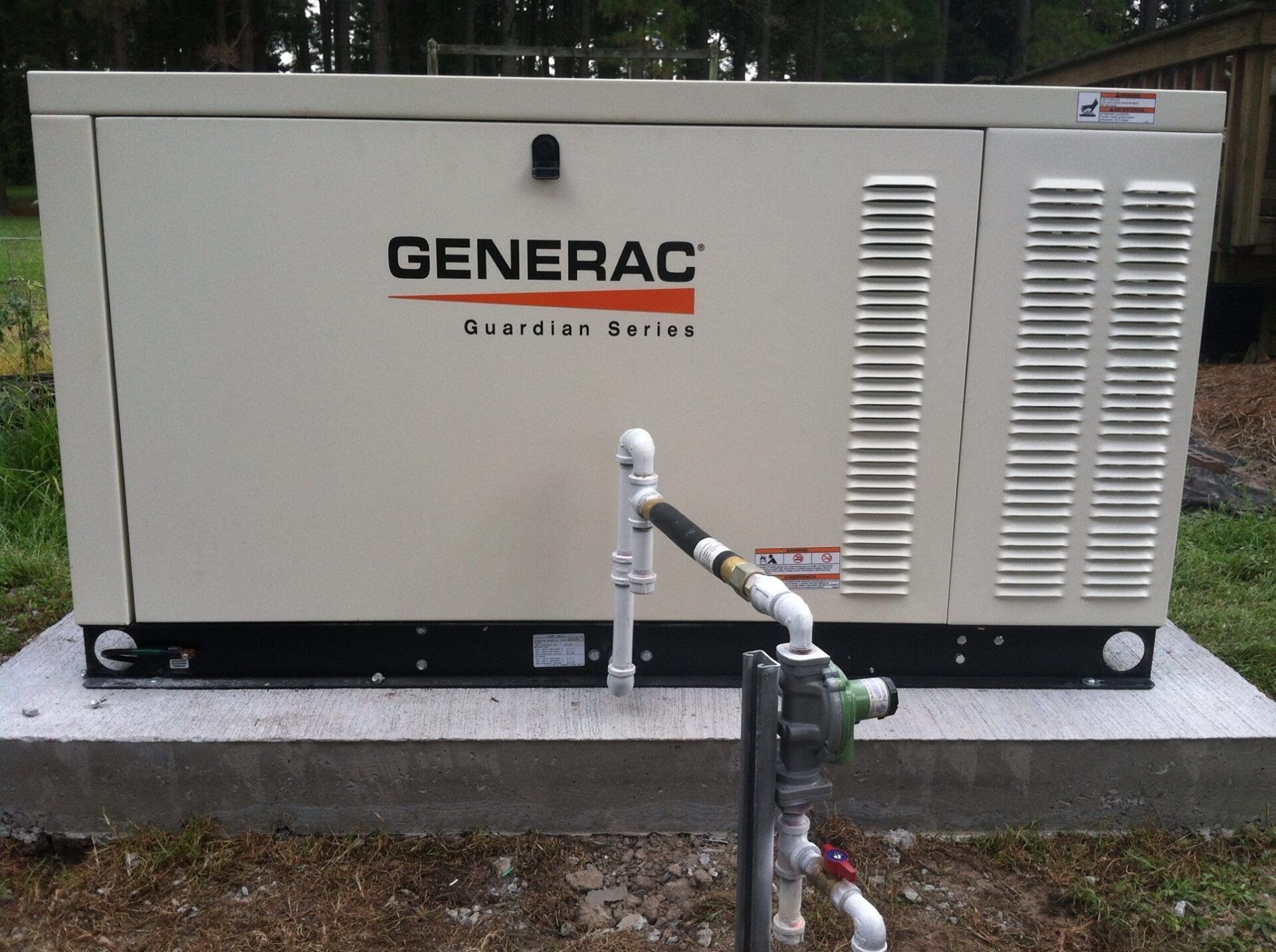 Generac Guardian Series generator on a concrete pad outdoors, with gas lines and vents.
