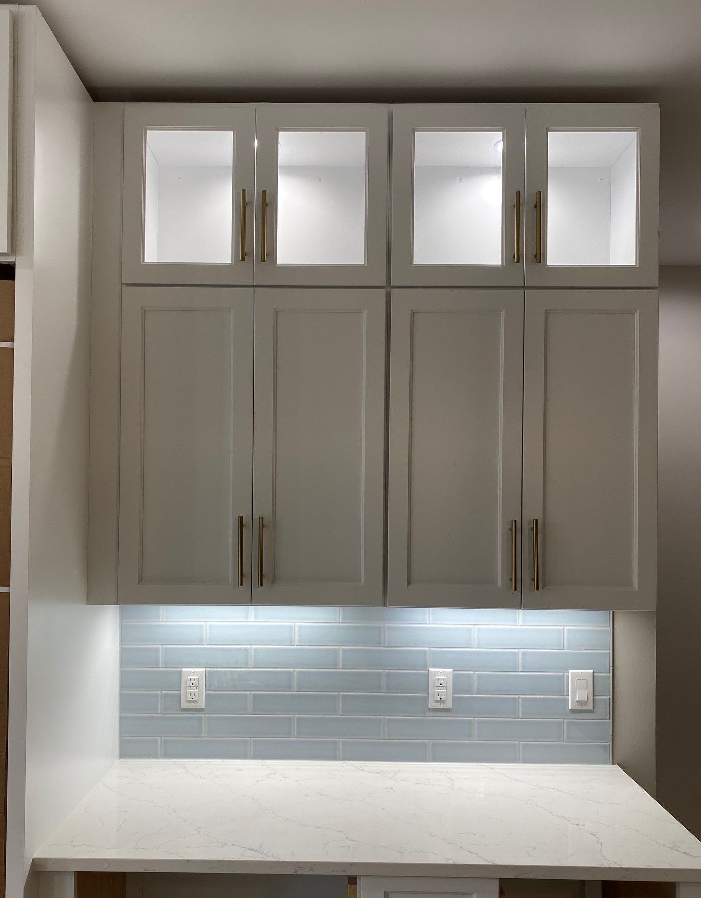 White built-in desk and cabinets with glass-paned doors and glowing lights.