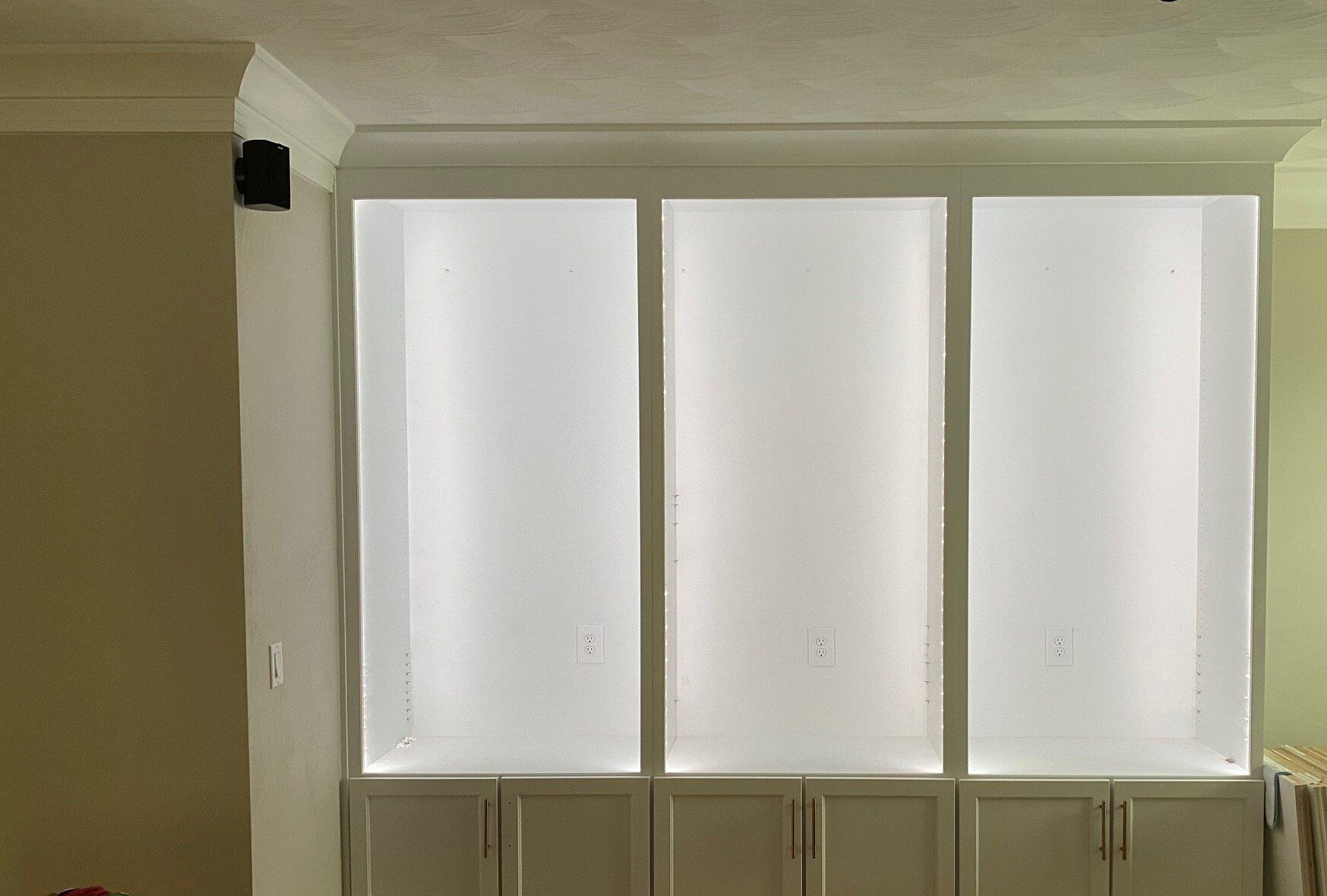 Built-in white cabinet with three frosted glass panels above lower storage cabinets, in a white-walled room.