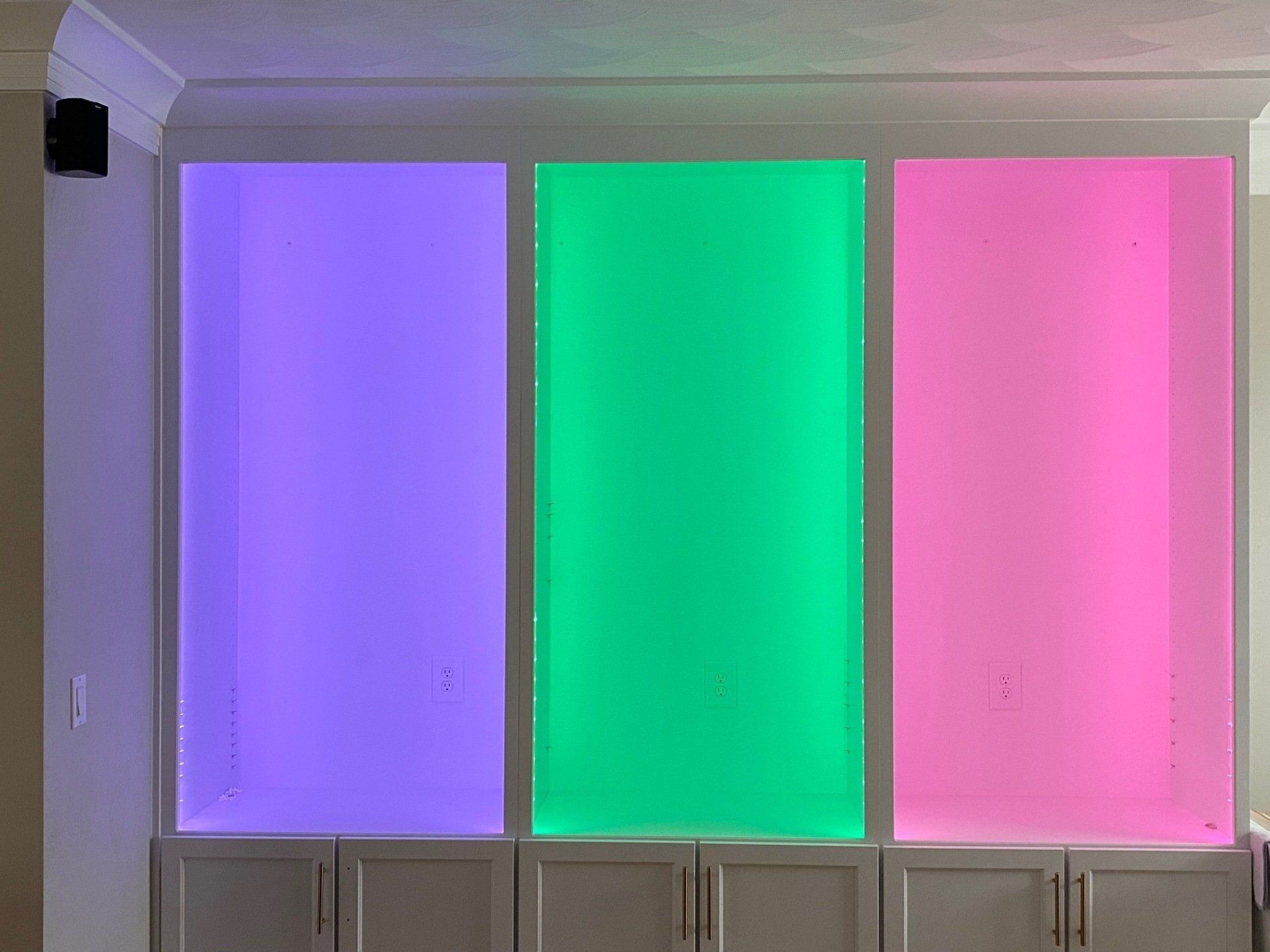 Three illuminated panels, purple, green, and pink, above white cabinets.