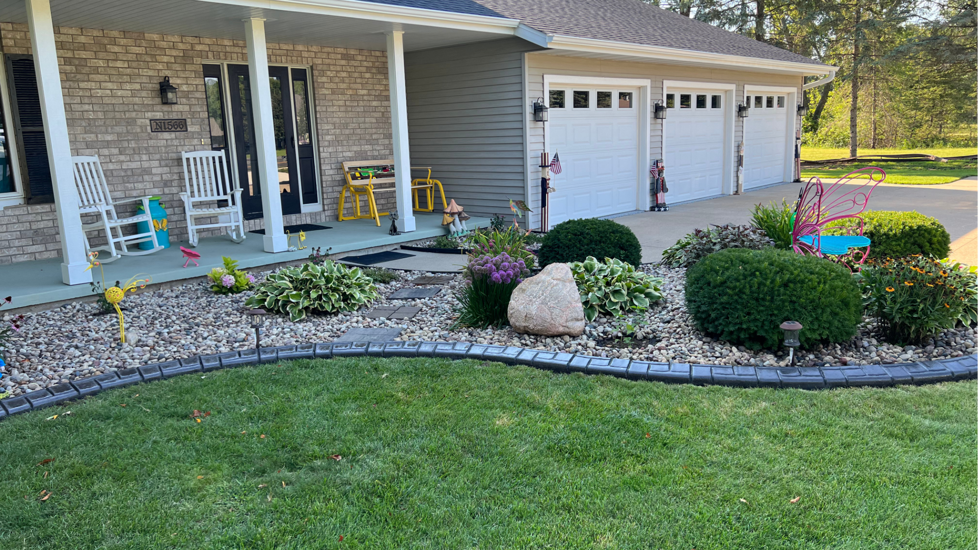 A house with a porch , rocking chairs , and a lush green lawn.