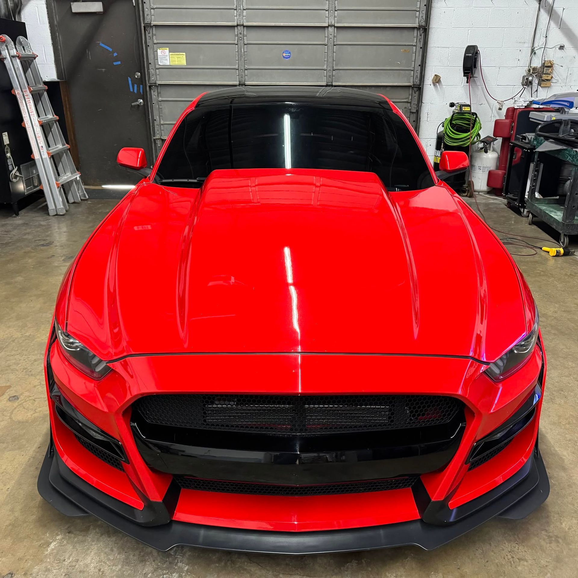 A red mustang is parked in a garage next to a garage door.