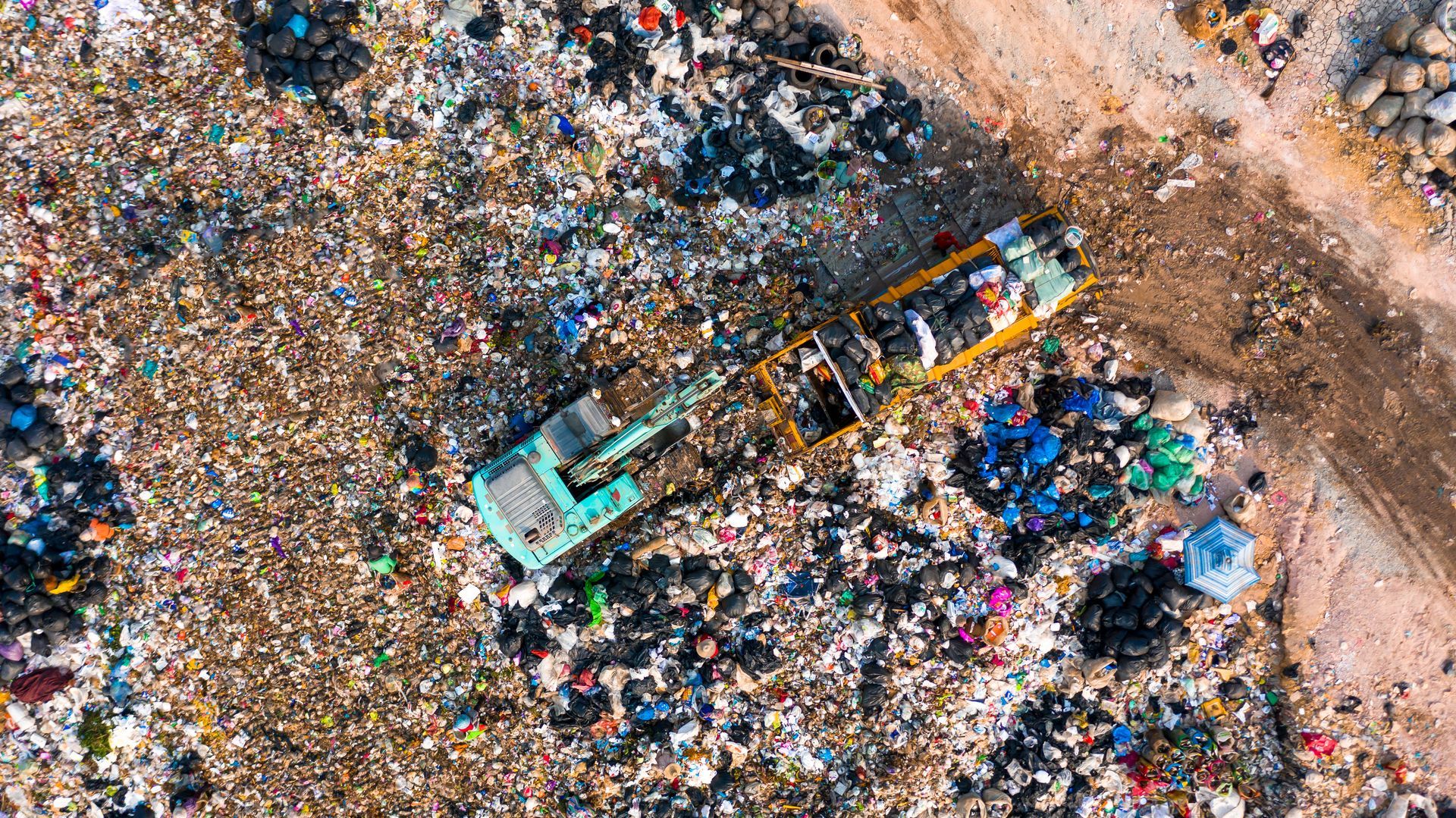 A large machine with a scoop unloads rubbish from a dump truck. Both are dwarfed by the surrounding landfill.