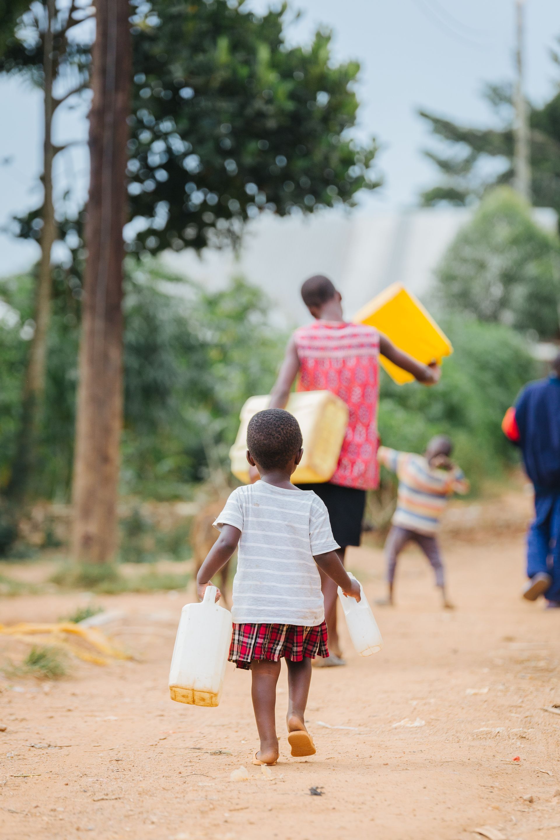 A family, including a young child no more than 6, walk down a beaten track to a well, clutching empty water cans in their hands.