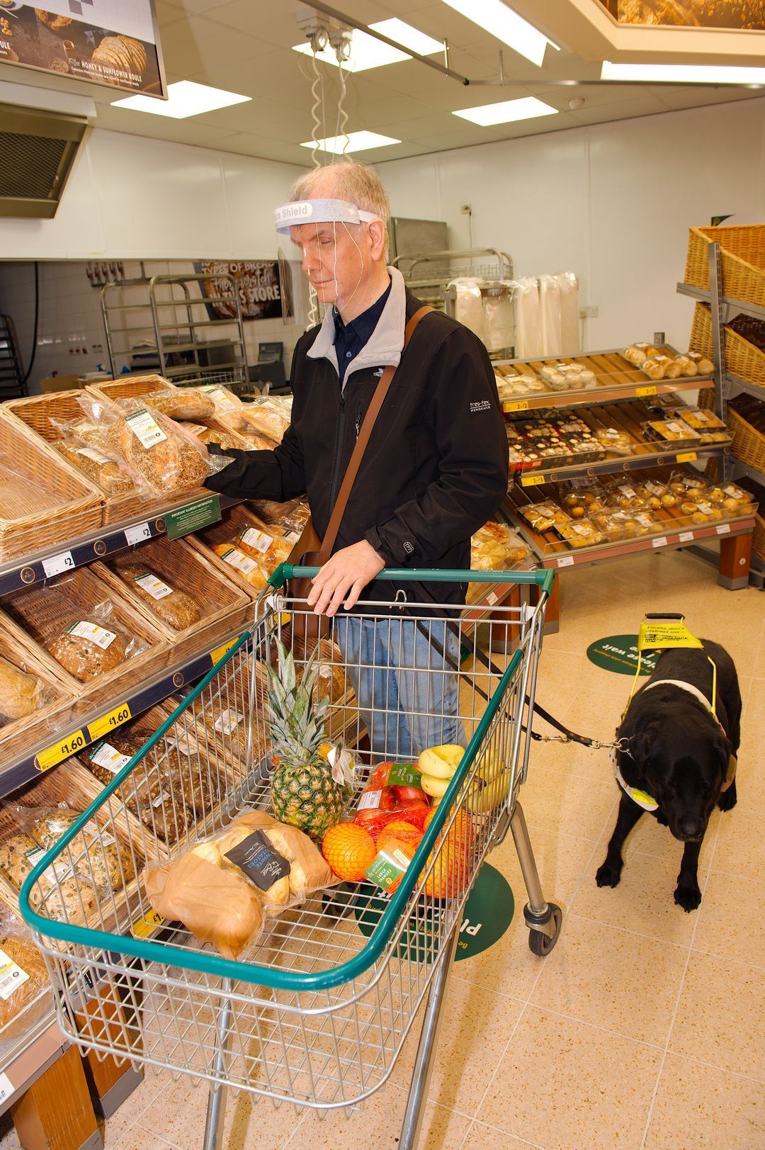 Philip selects a crusty loaf in the bread aisle and adds it to his shopping trolley.