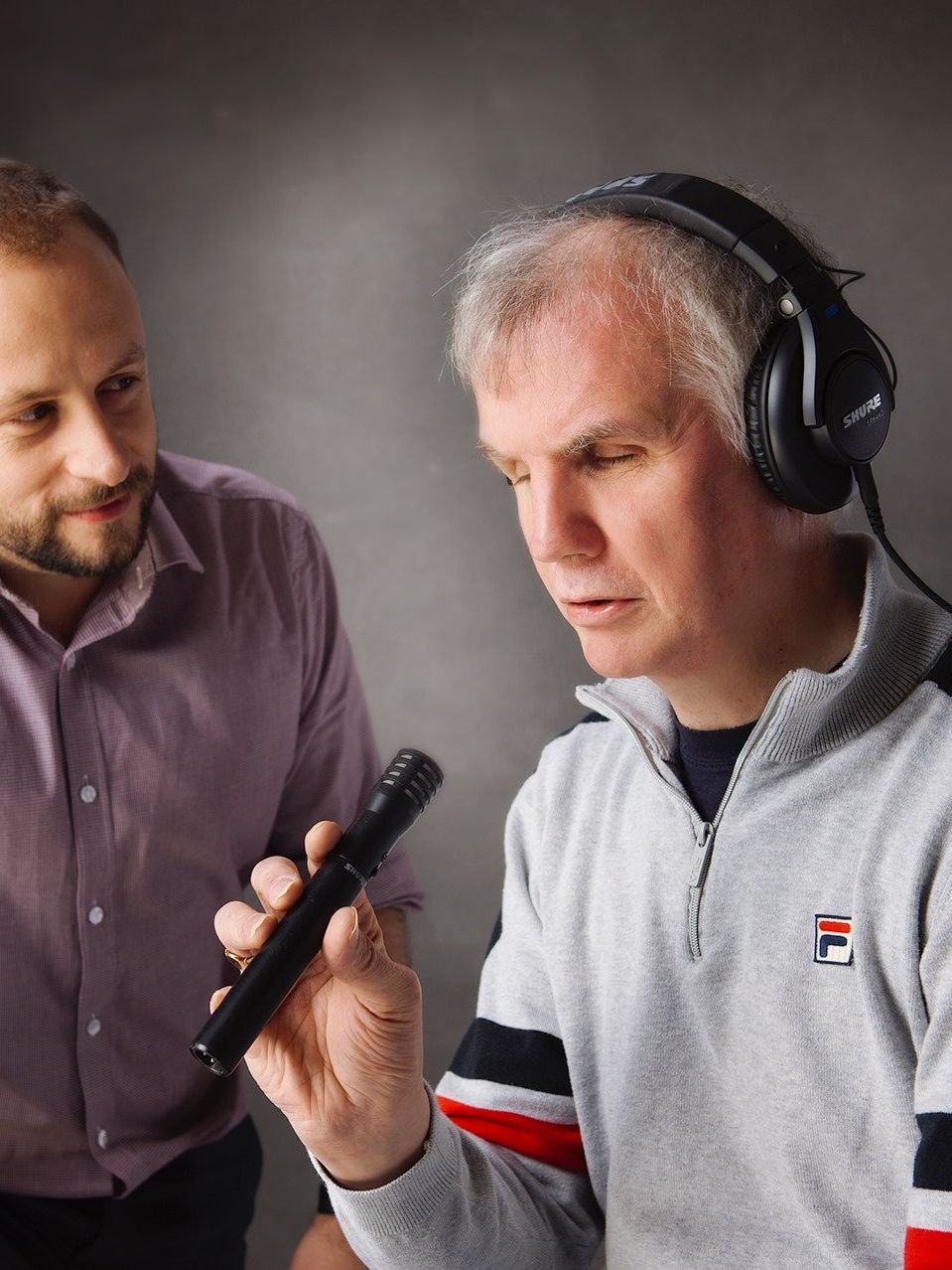 Photograph of Philip Anderson, wearing headphones and holding microphone, conducting a radio interview independently on location.