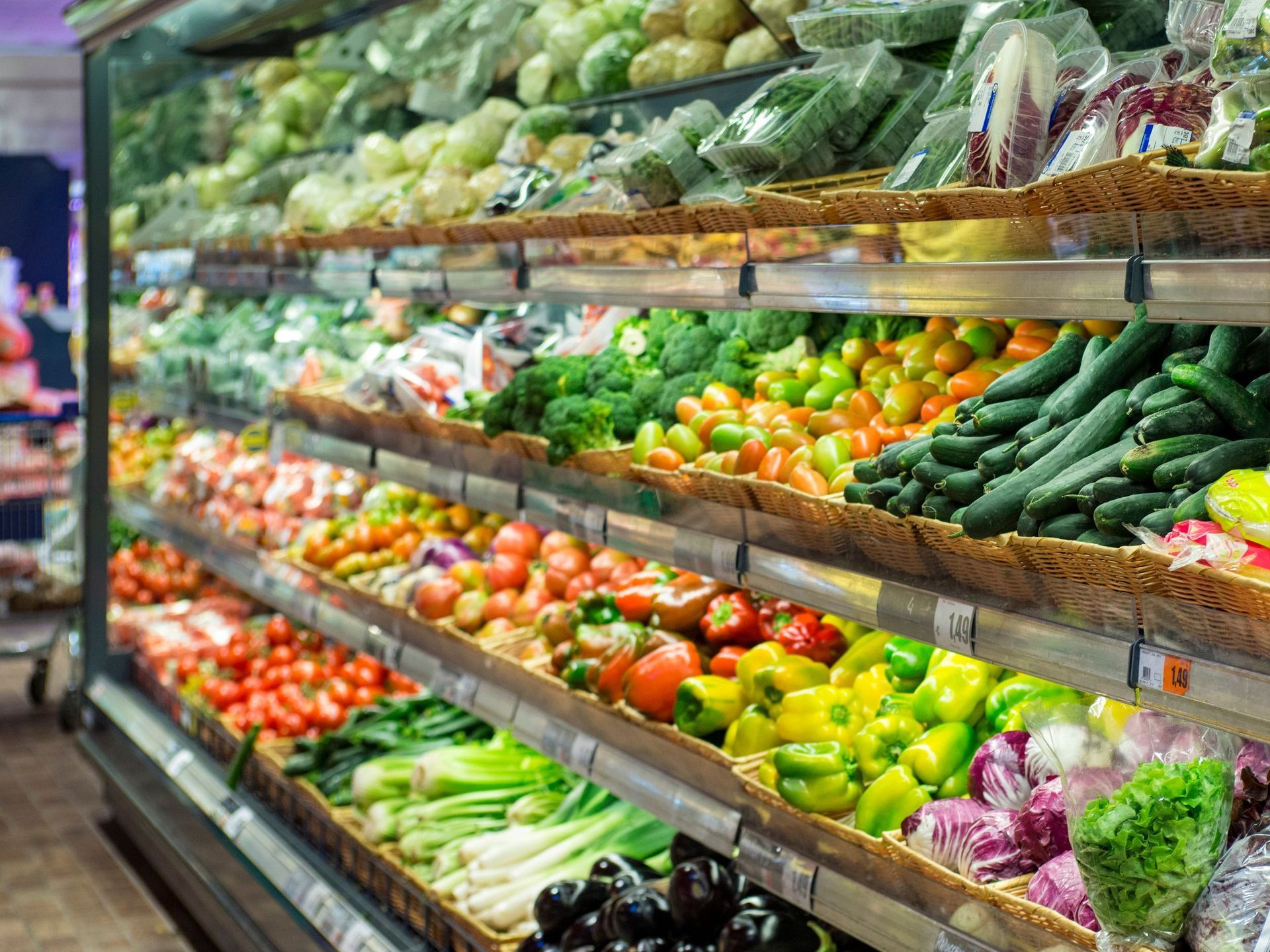 (Inclusive Product Labelling) An array of vegetables on supermarket shelves, cluttered together in baskets without distinct labels.