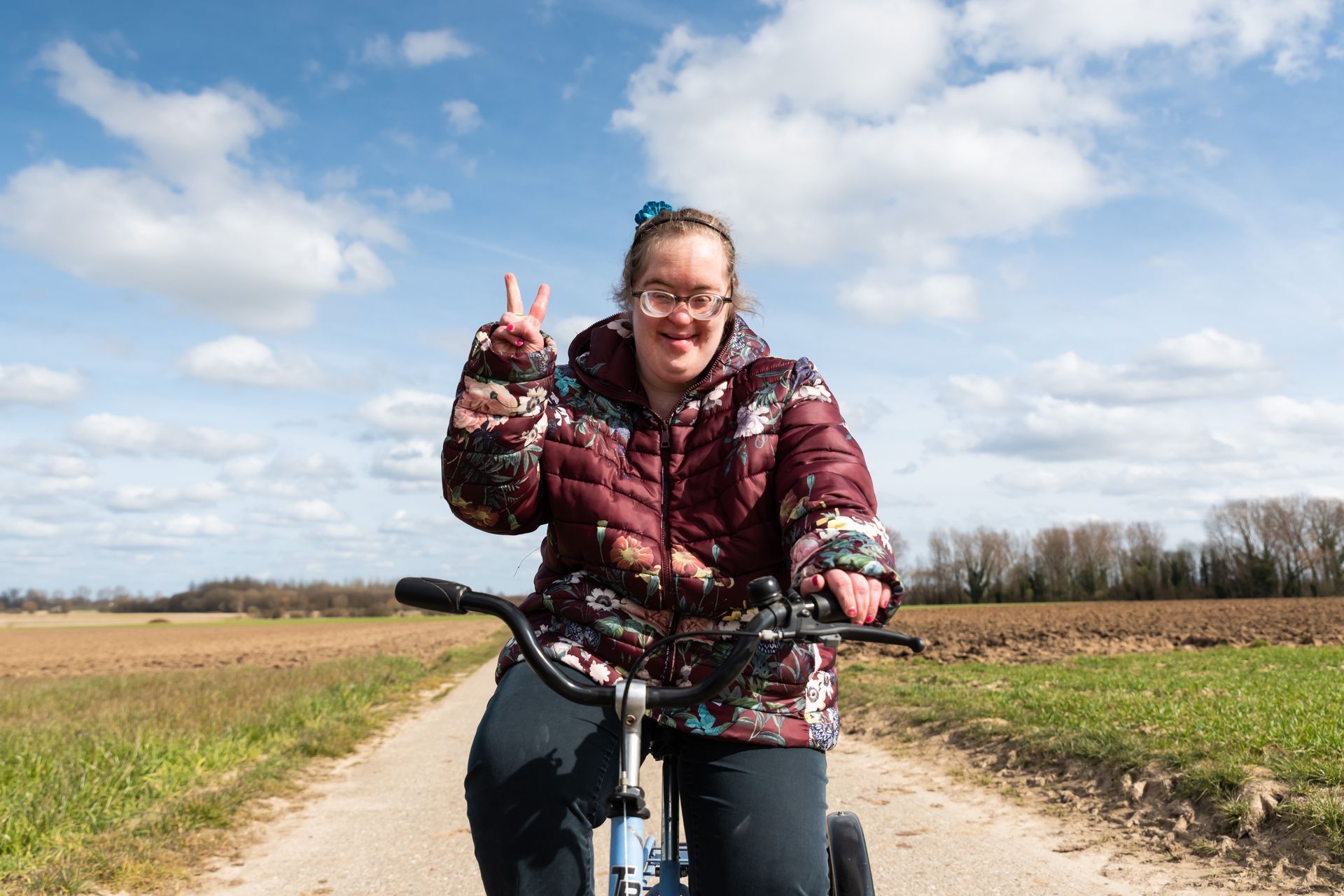 A young woman with Down Syndrome smiles as she rides her bike through some fields. 