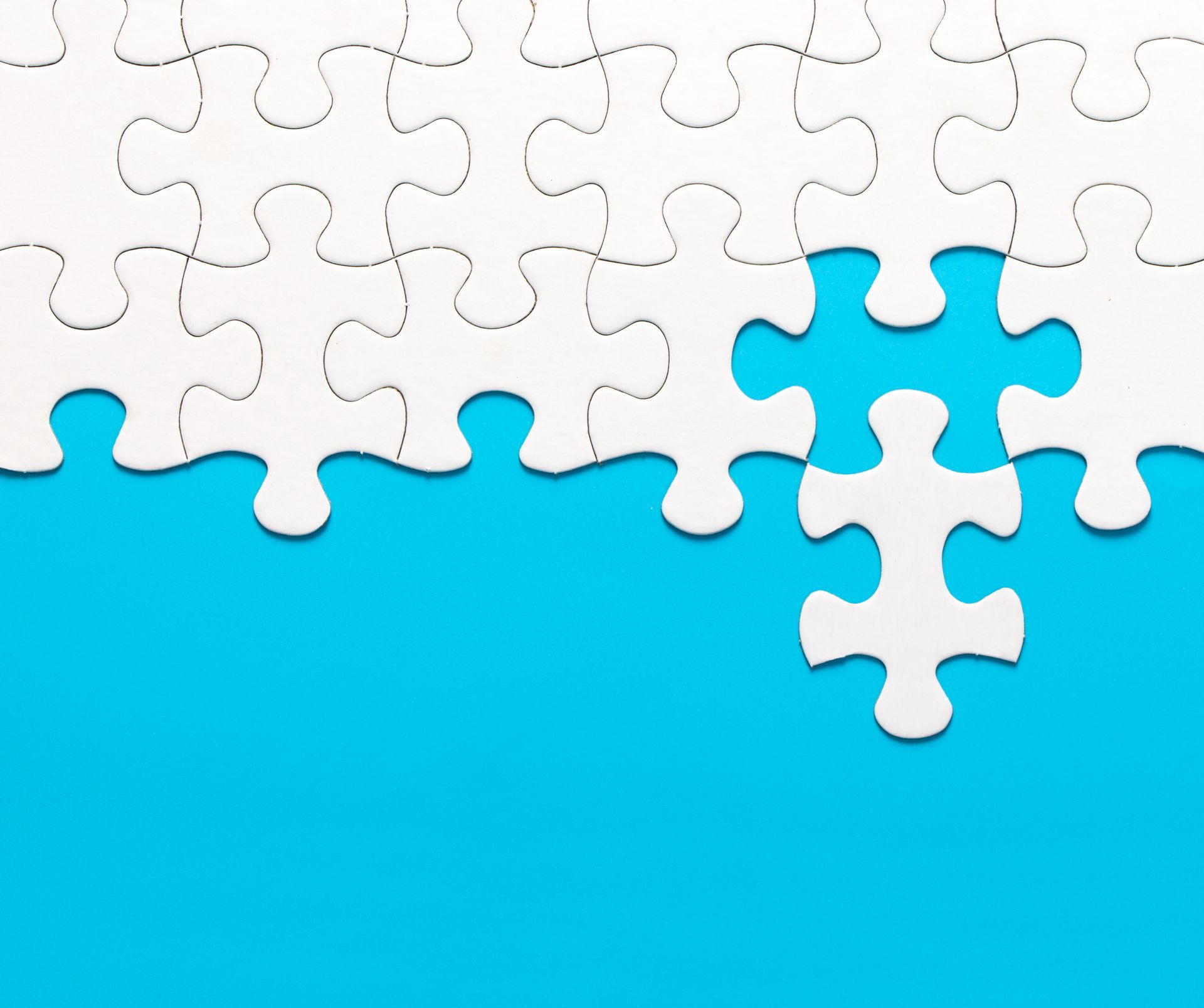 A white puzzle is mostly complete on a blue background. One small piece however stands out from the rest.