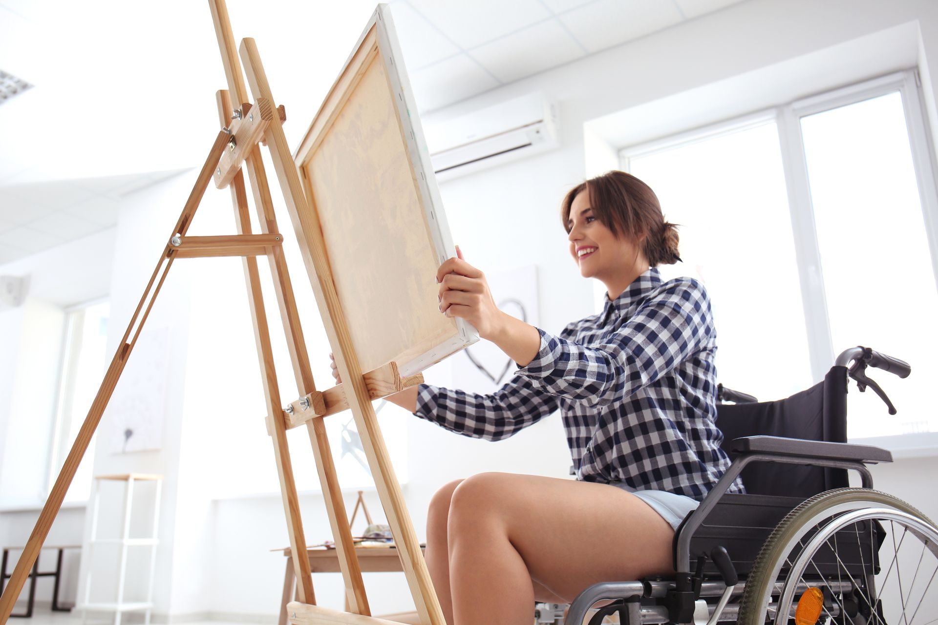 A young woman in a wheelchair beams as she places a canvas on an easel.