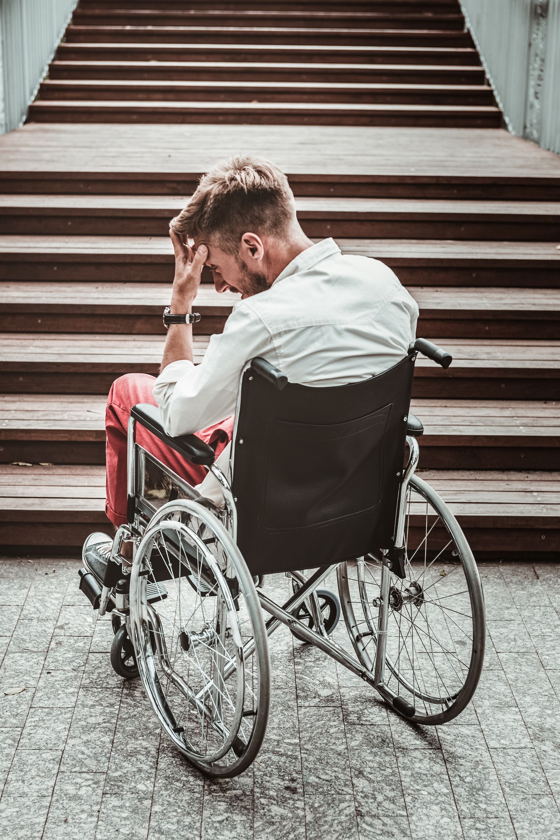 A man in a wheelchair hangs his head in disappointment as he's faced with stairs without wheelchair access.