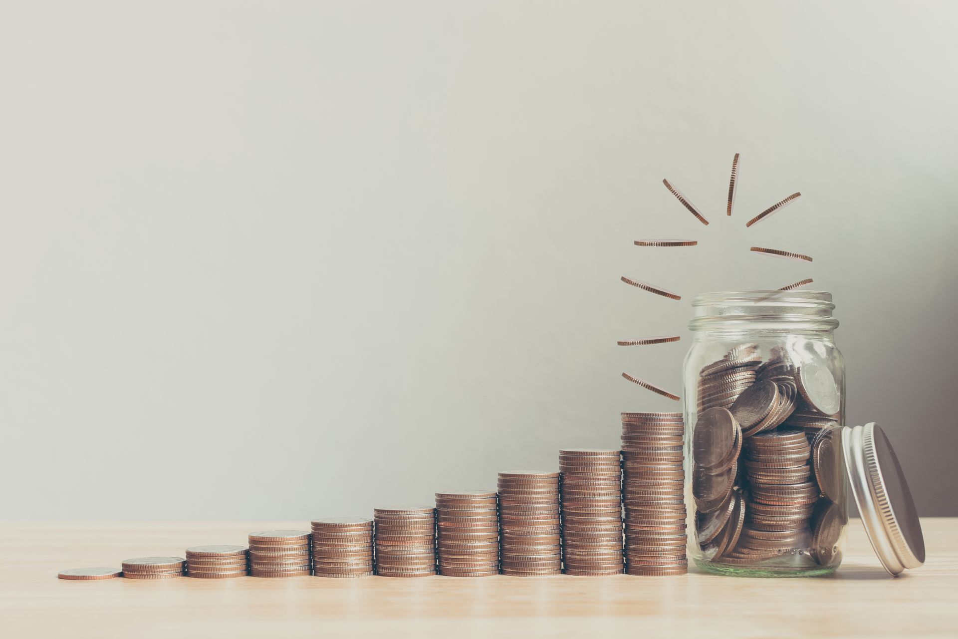 A series of stacks of coins, each increasing as they move towards a jar filled with coins. 