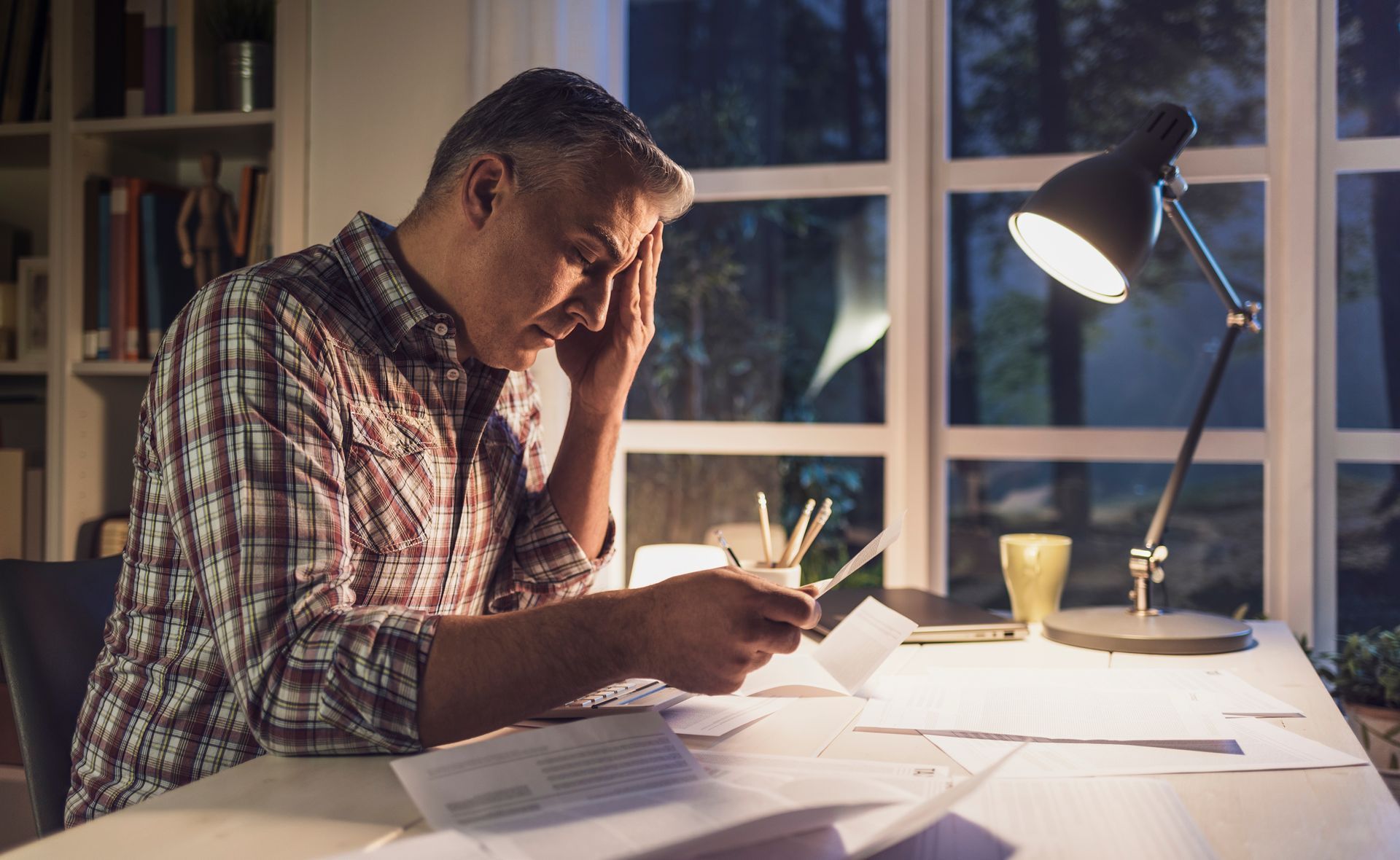 Photograph of a tired man sitting at his desk reviewing financial paperwork.