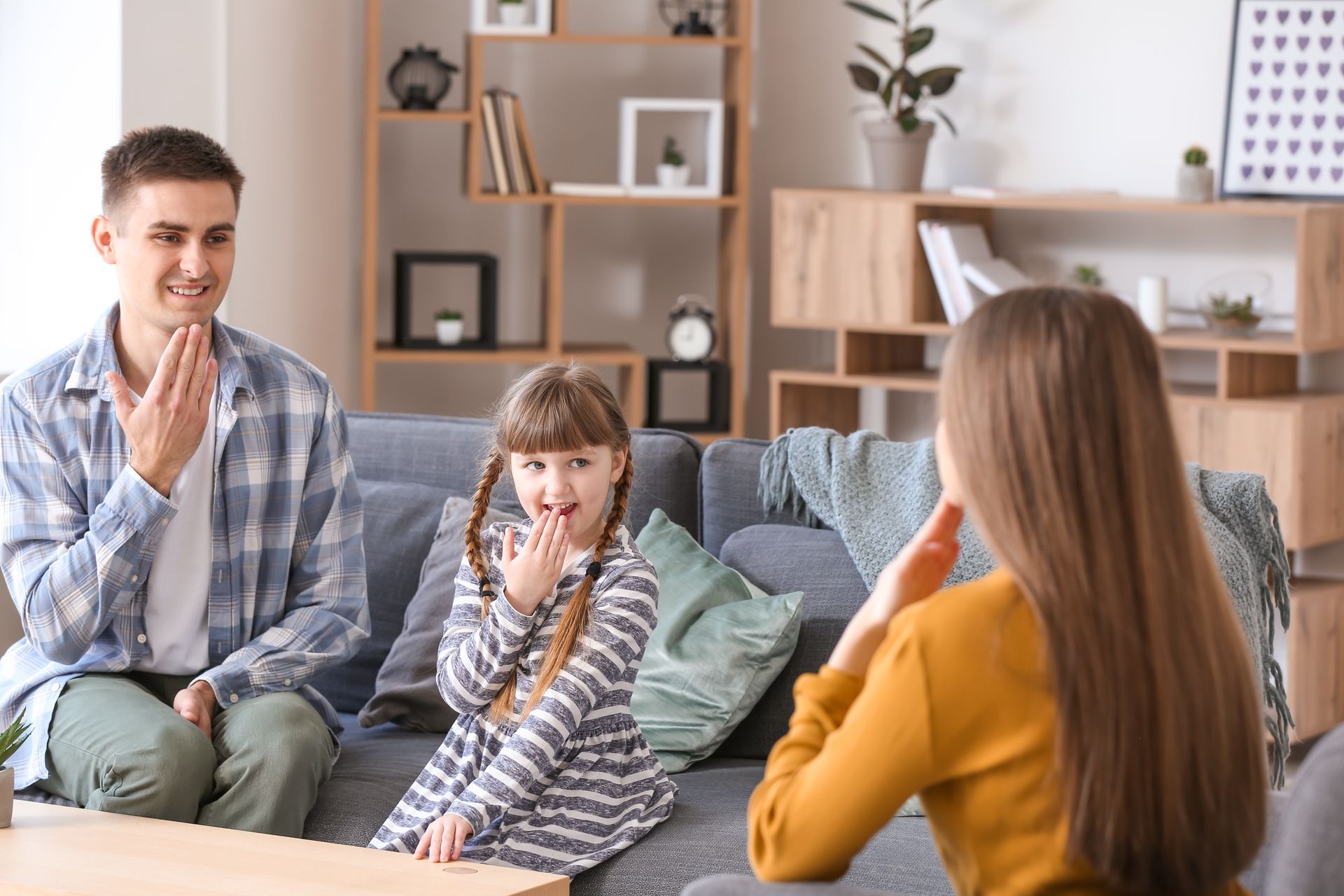 A family sitting in a living room practice sign language while sat on the sofa.