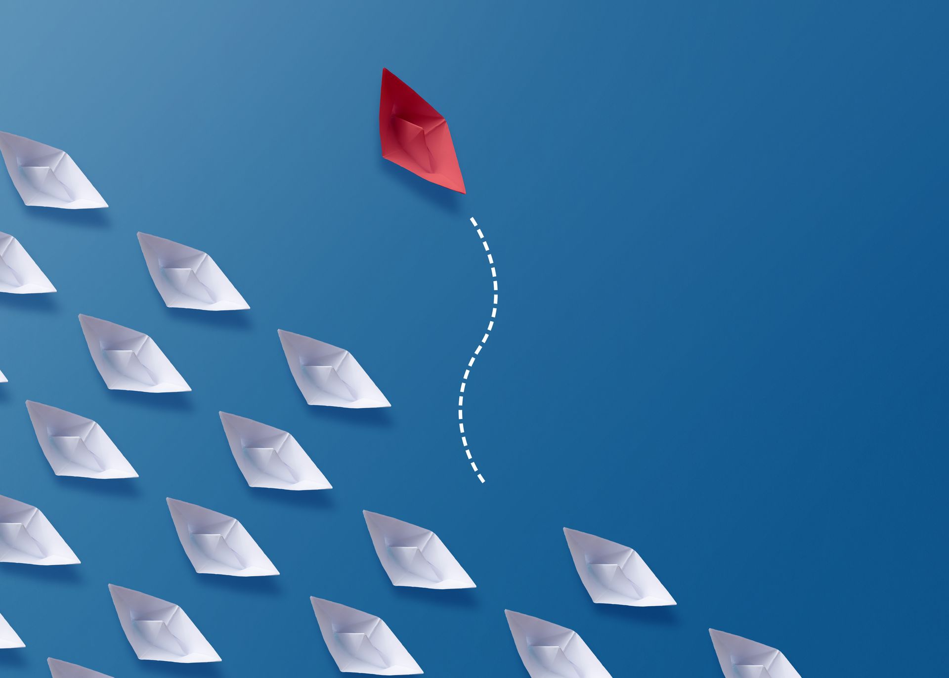 A convoy of white paper boats sails in a single direction, but a little red paper boat escapes its row to forge its own path.