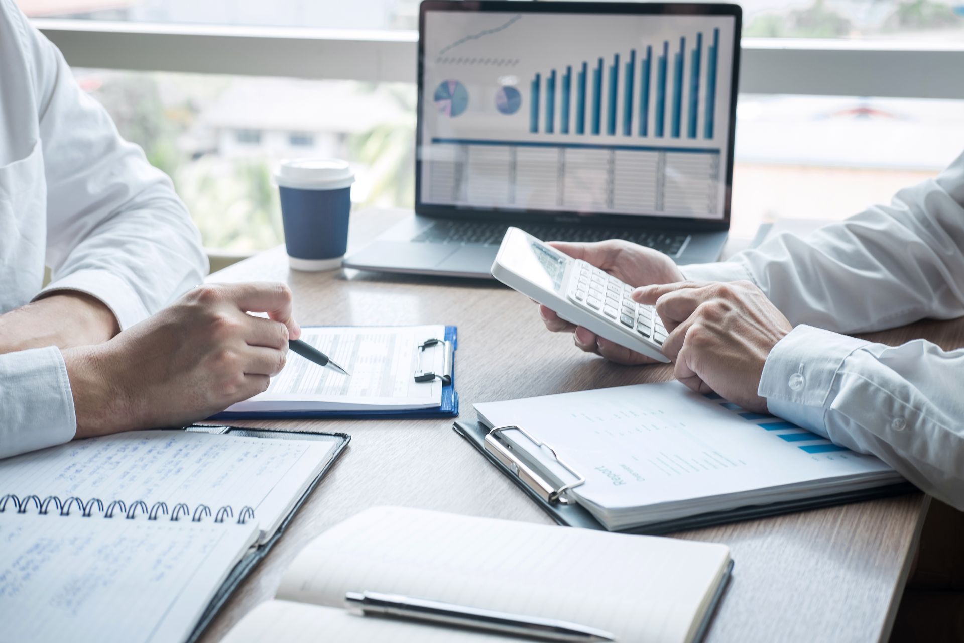 Photo of two people in suits at a desk, one is holding a pen, the other is using a calculator.