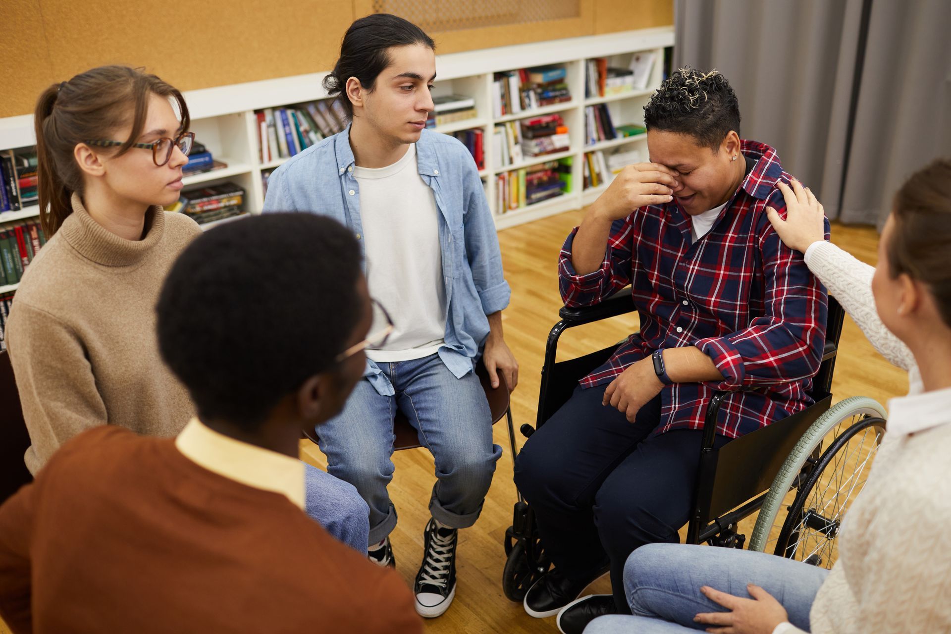 (Community Engagement) A group of people sit in a circle, listening to and supporting a woman in a wheelchair as she gives feedback and cries.