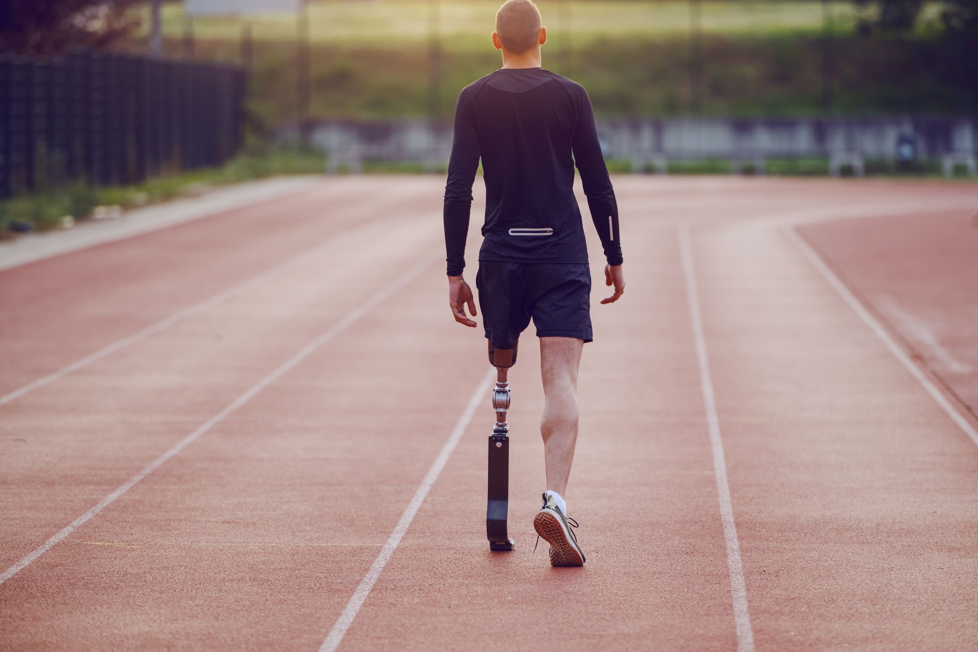An athletic man with a prosthetic running leg prepares to run on a marathon track.