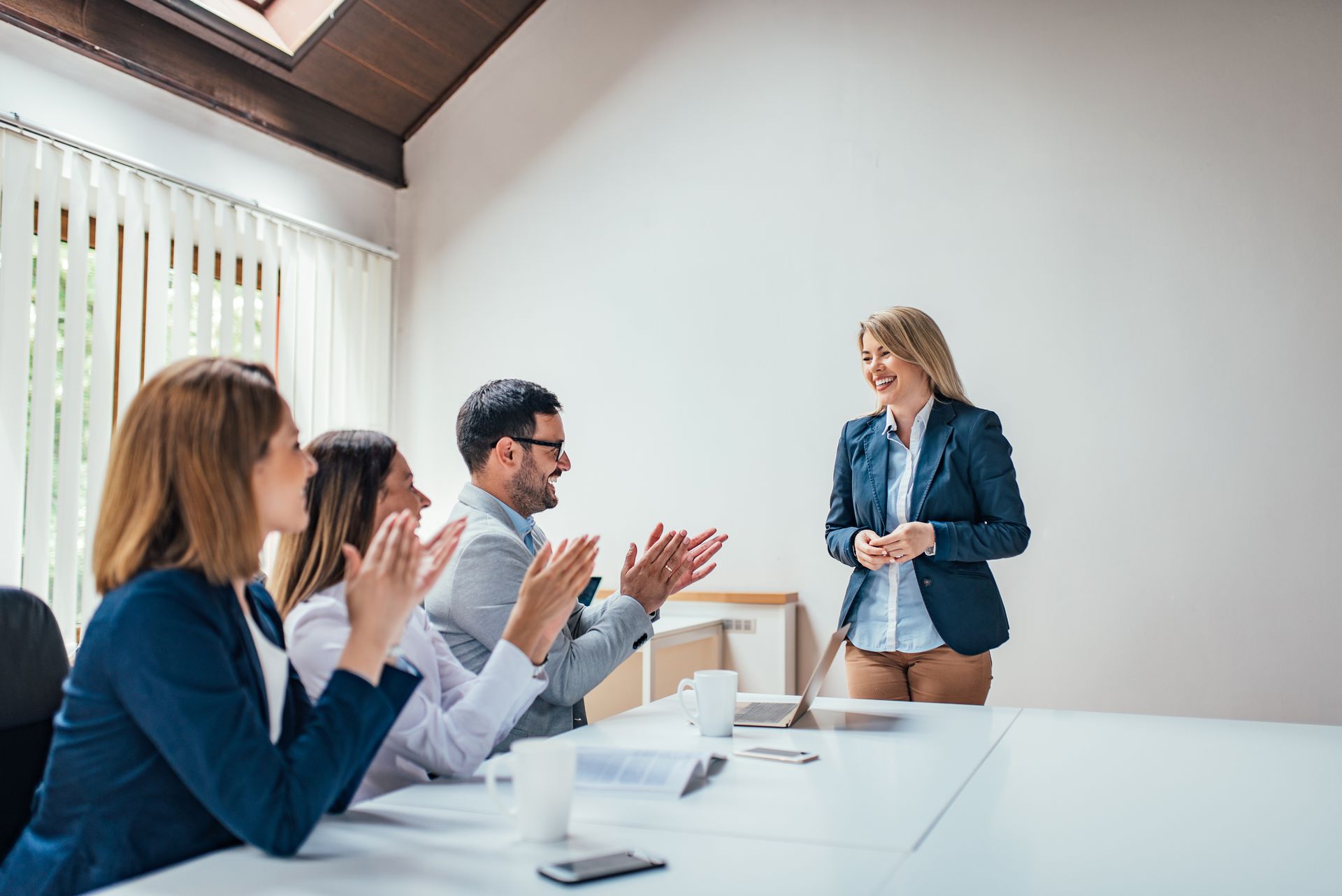 A woman presents to several applauding colleagues in a conference room. 