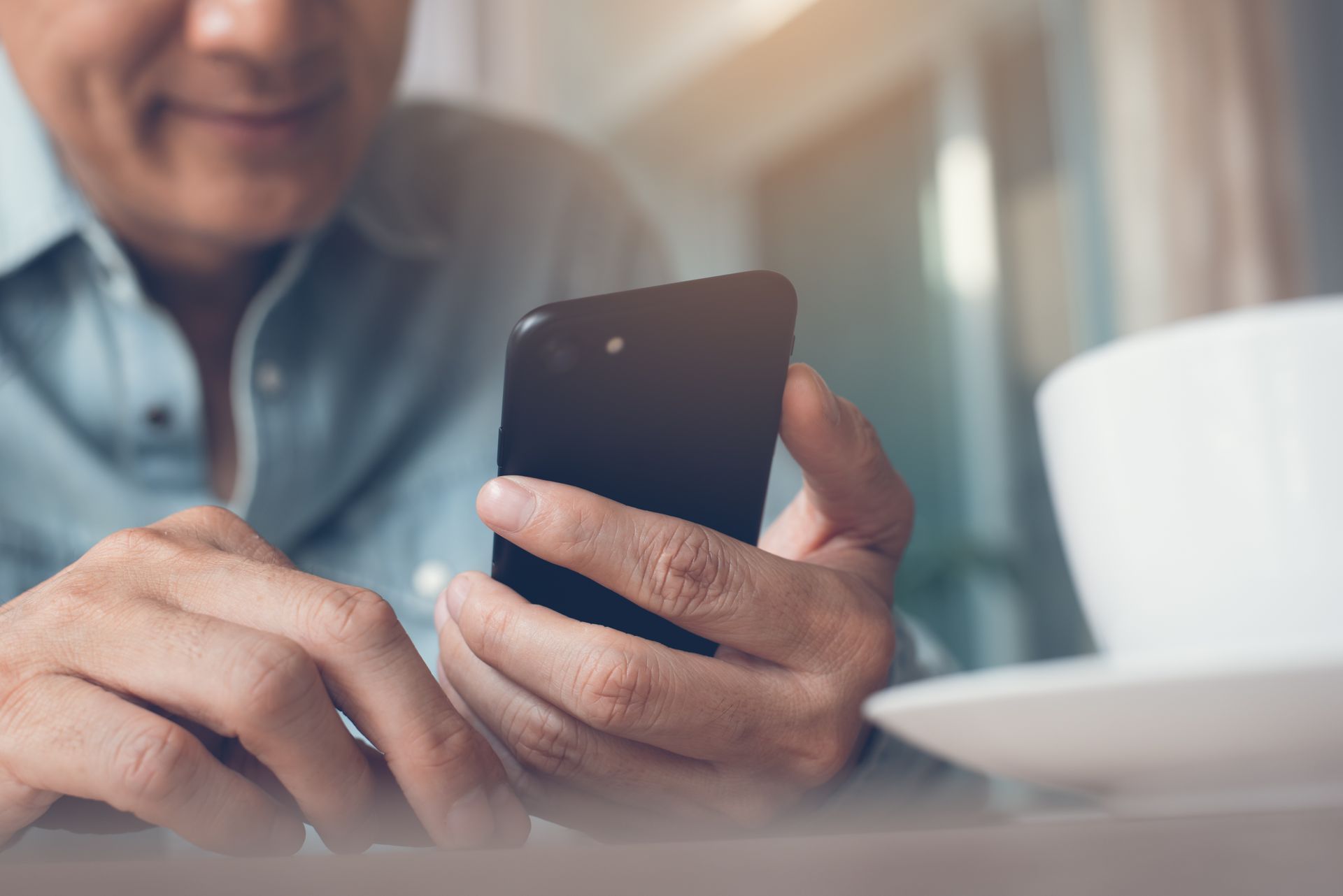 Photograph of a man holding a smartphone, looking at it and smiling. 