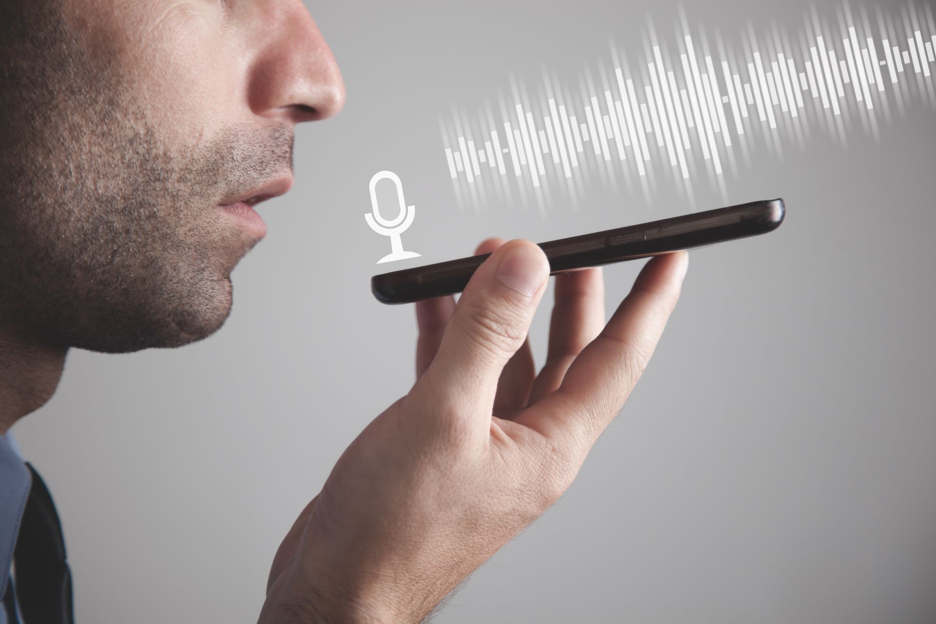 A man in a suit holds his phone up to his face as he speaks into it. His voice is represented by a series of gradually changing lines as he uses the voice recognition software..