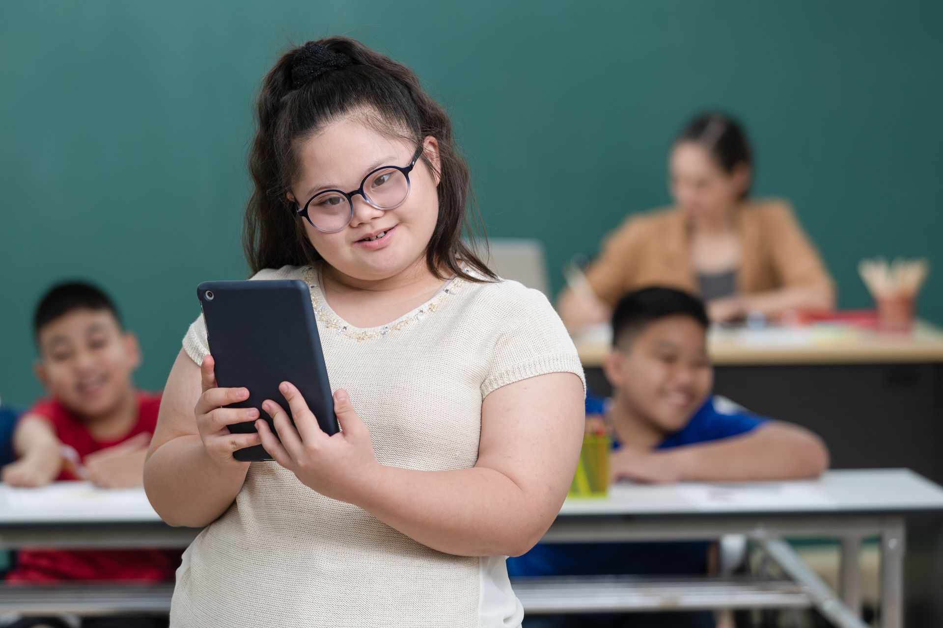 A young girl with Down Syndrome smiles as she uses a tablet in her classroom.