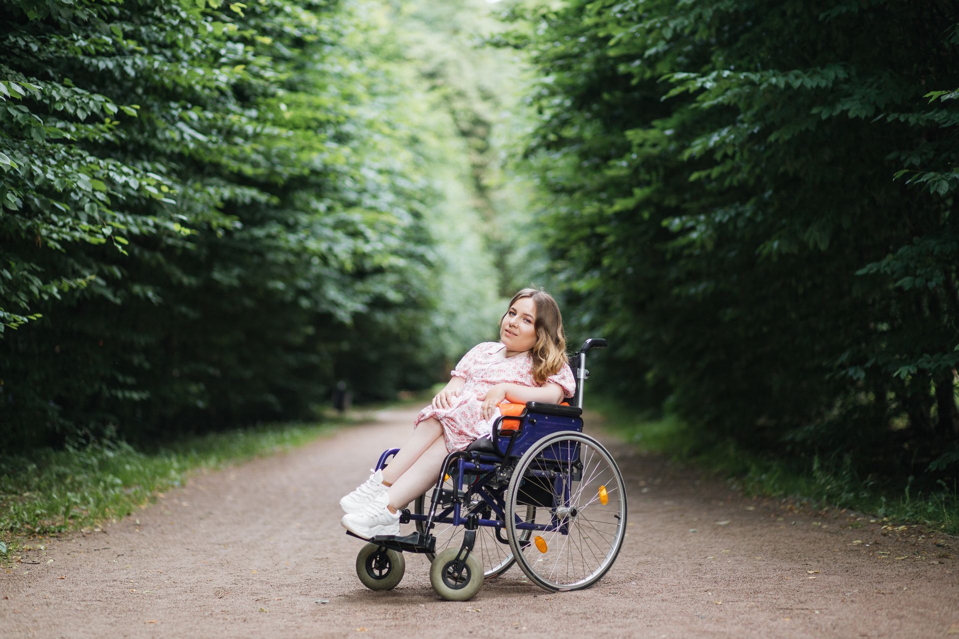 A smiling woman in a wheelchair enjoys a bright and sunny day in the park.