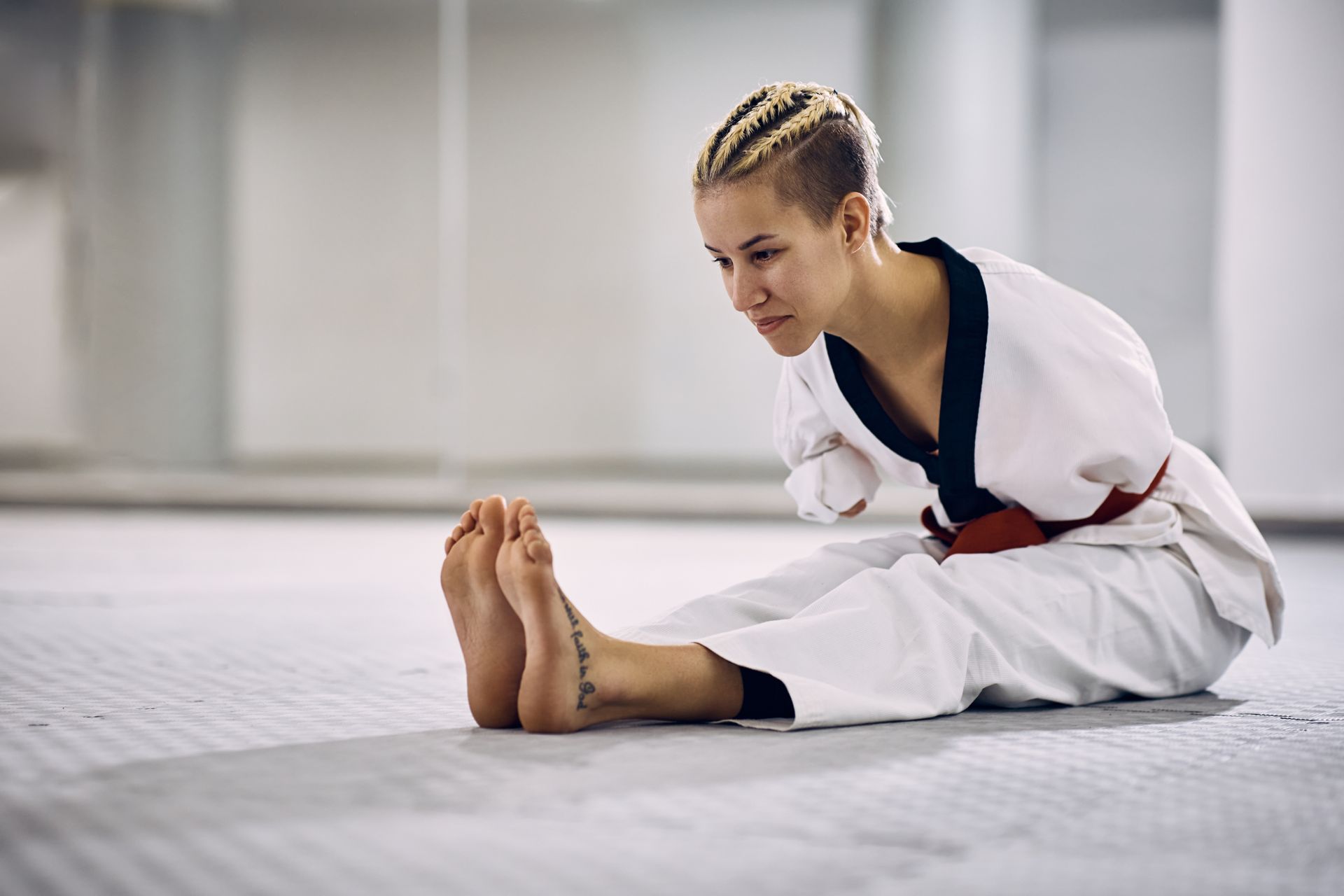 A female para-athlete stretches on the floor before taekwondo training.