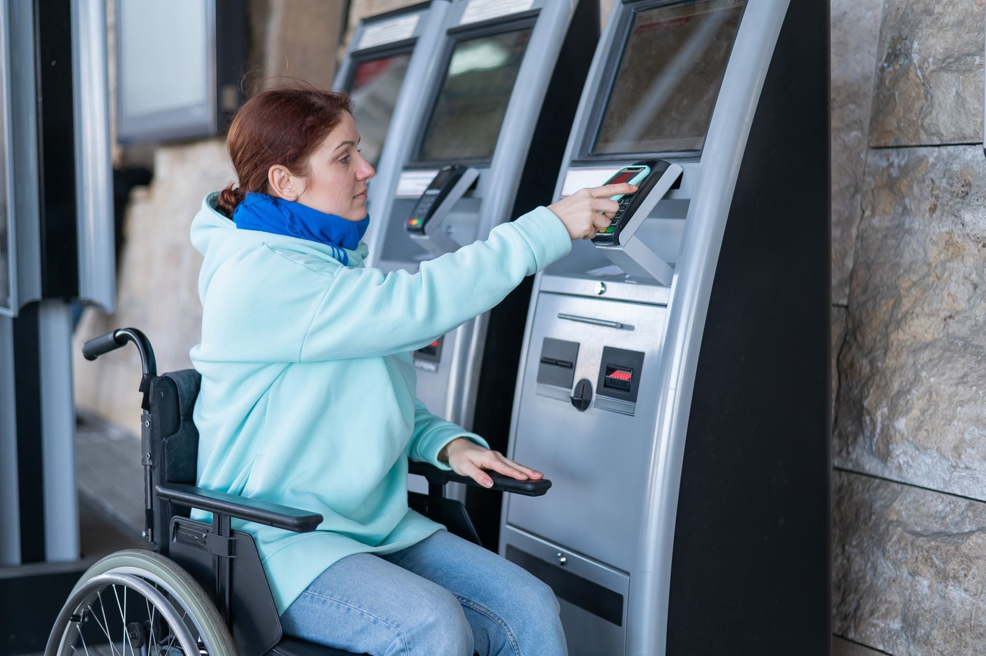 A woman in a wheelchair pays for train tickets at a digital kiosk.