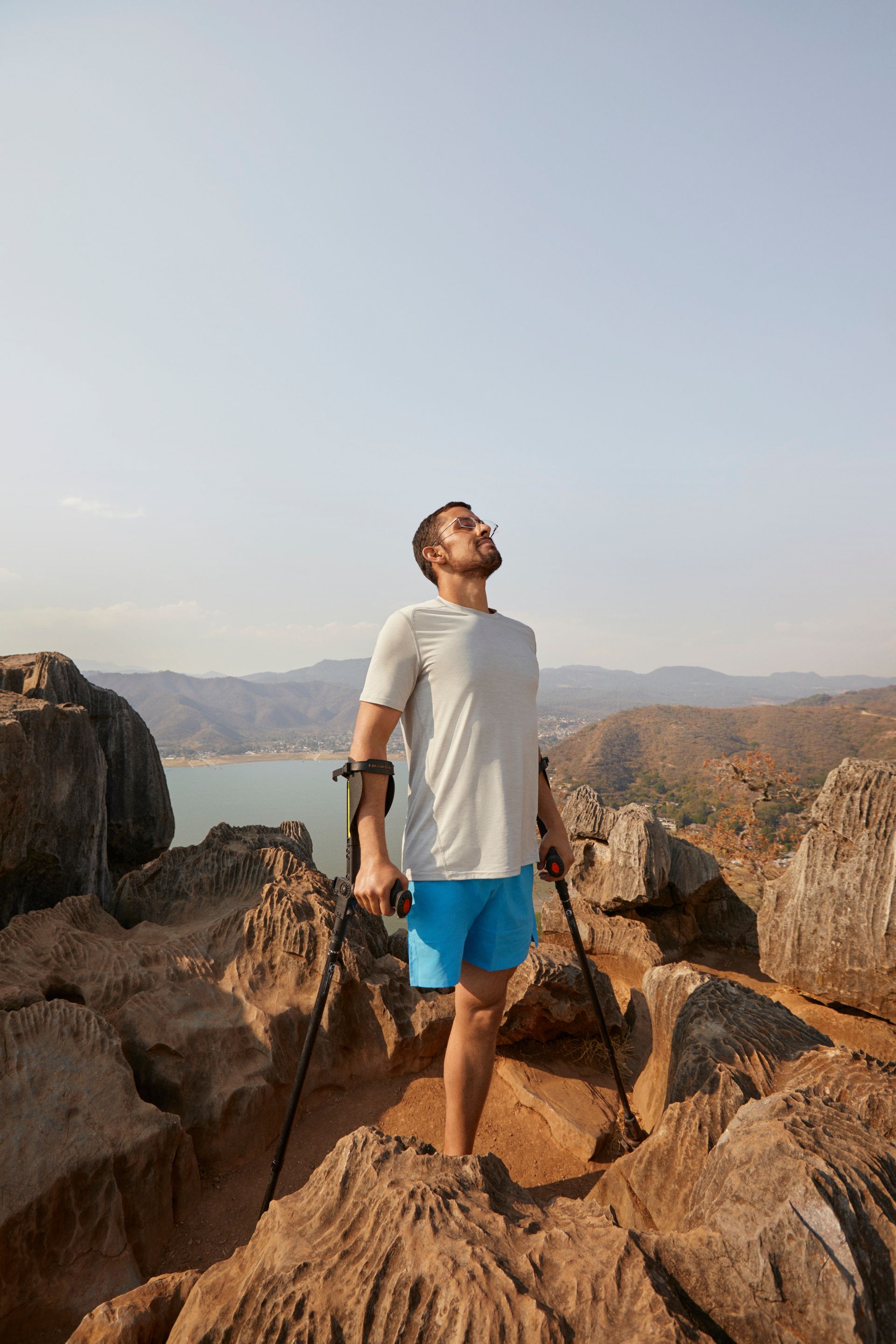 On an high, rocky outcrop, a man with crutches and a lower limb amputation breathes in the fresh air after a long climb. 