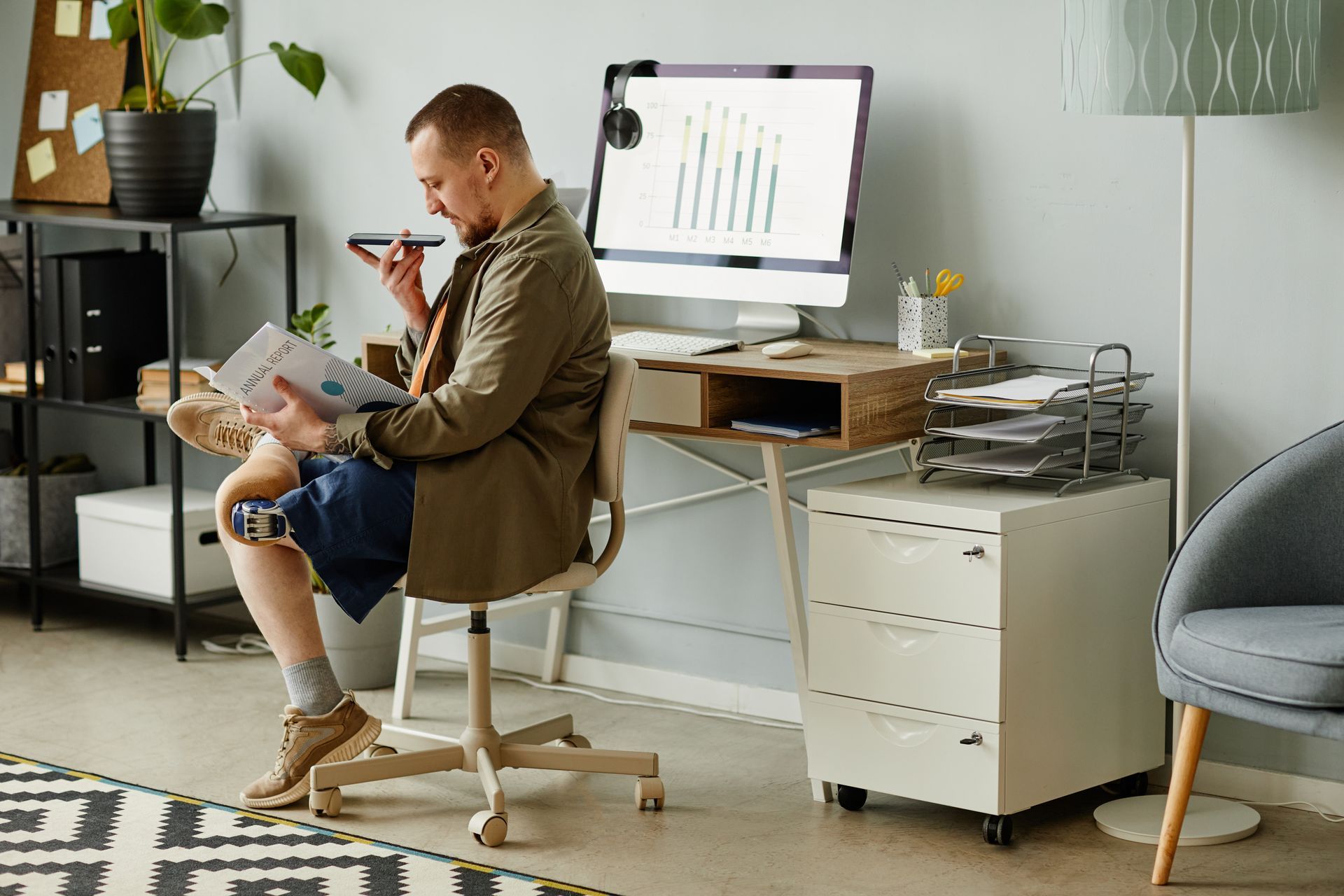 A man with a prosthetic leg sits at a desk while speaking directly into his phone. 