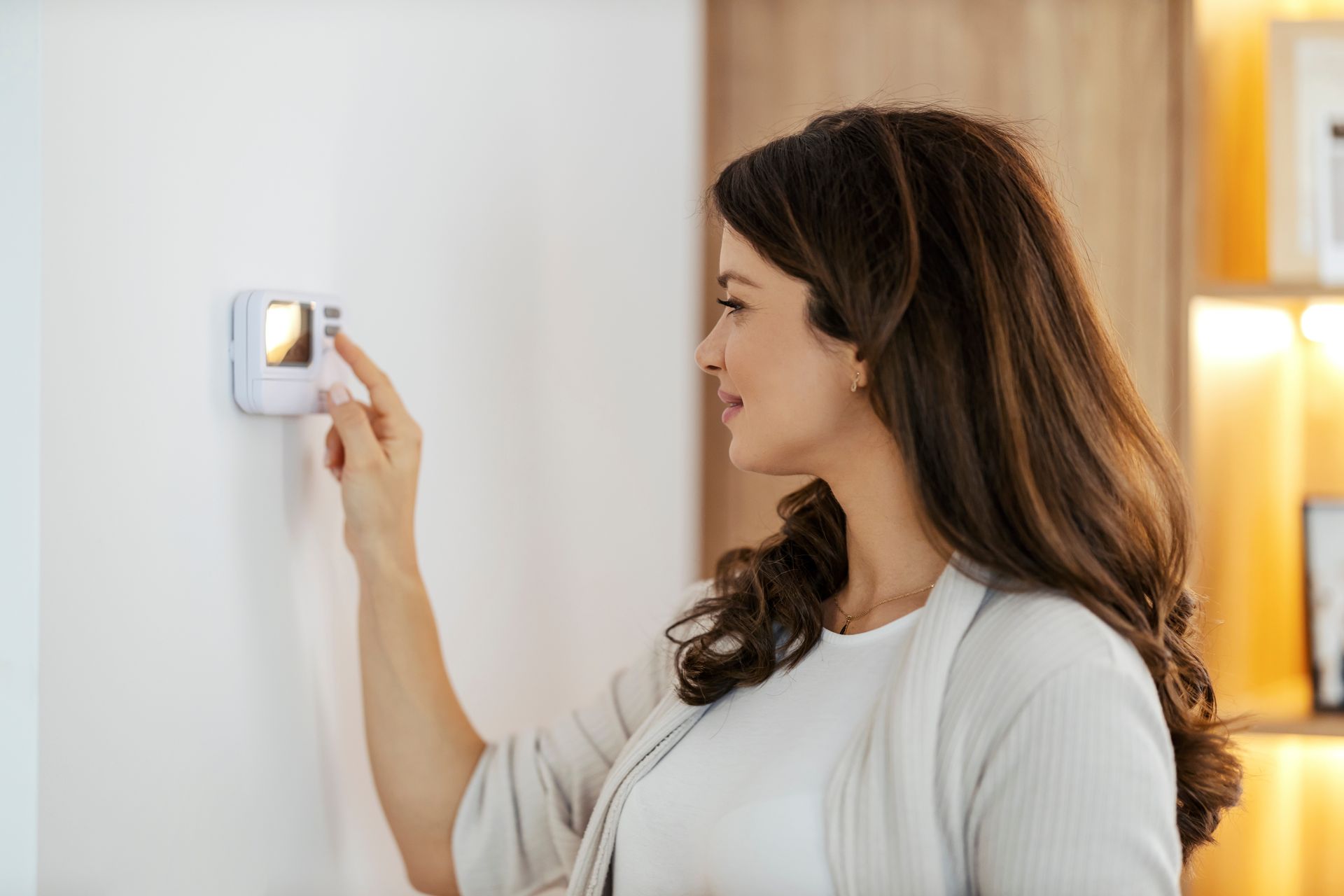 Photo of a woman adjusting a digital thermostat.